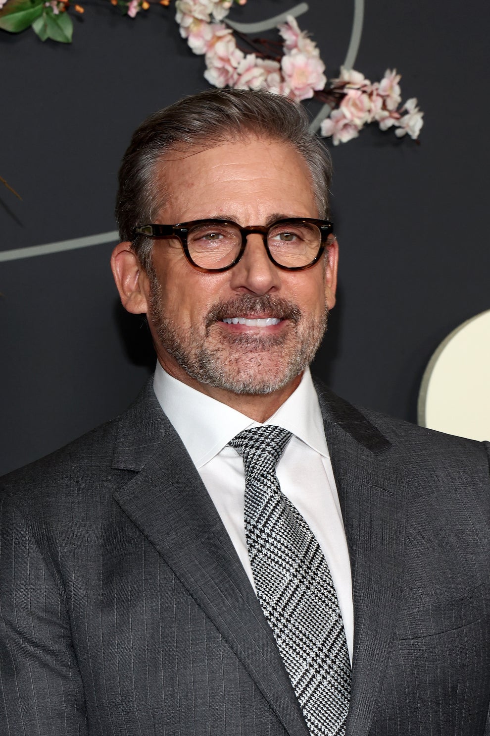 21 Jaw-Dropping "Then And Now" Photos Of Celebrities Who Have Gotten Wayyyyy Sexier With Age 42 Man in glasses wearing a grey suit and checkered tie, smiling at an event