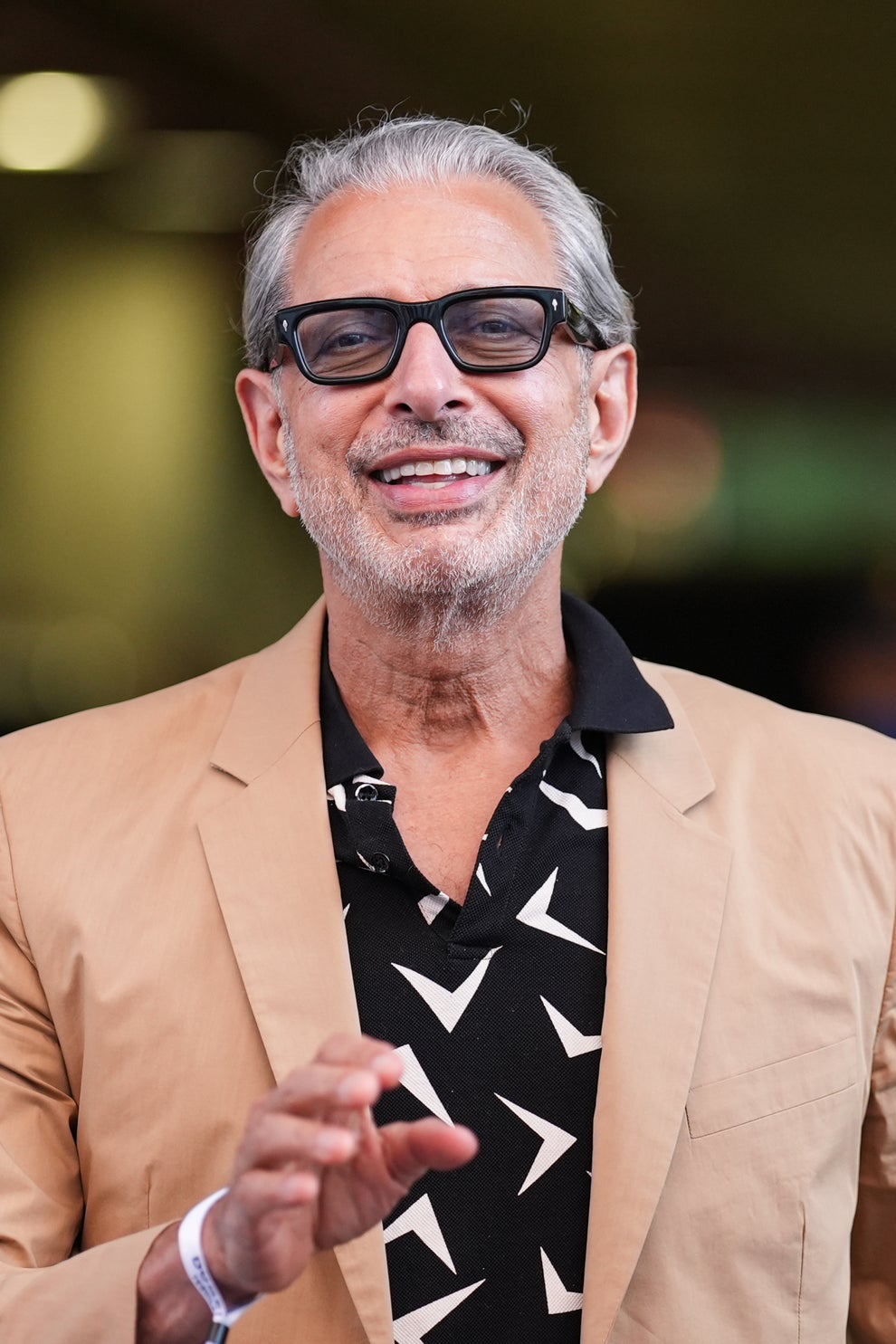 21 Jaw-Dropping "Then And Now" Photos Of Celebrities Who Have Gotten Wayyyyy Sexier With Age 72 Man in a beige jacket with a patterned black shirt, smiling and gesturing