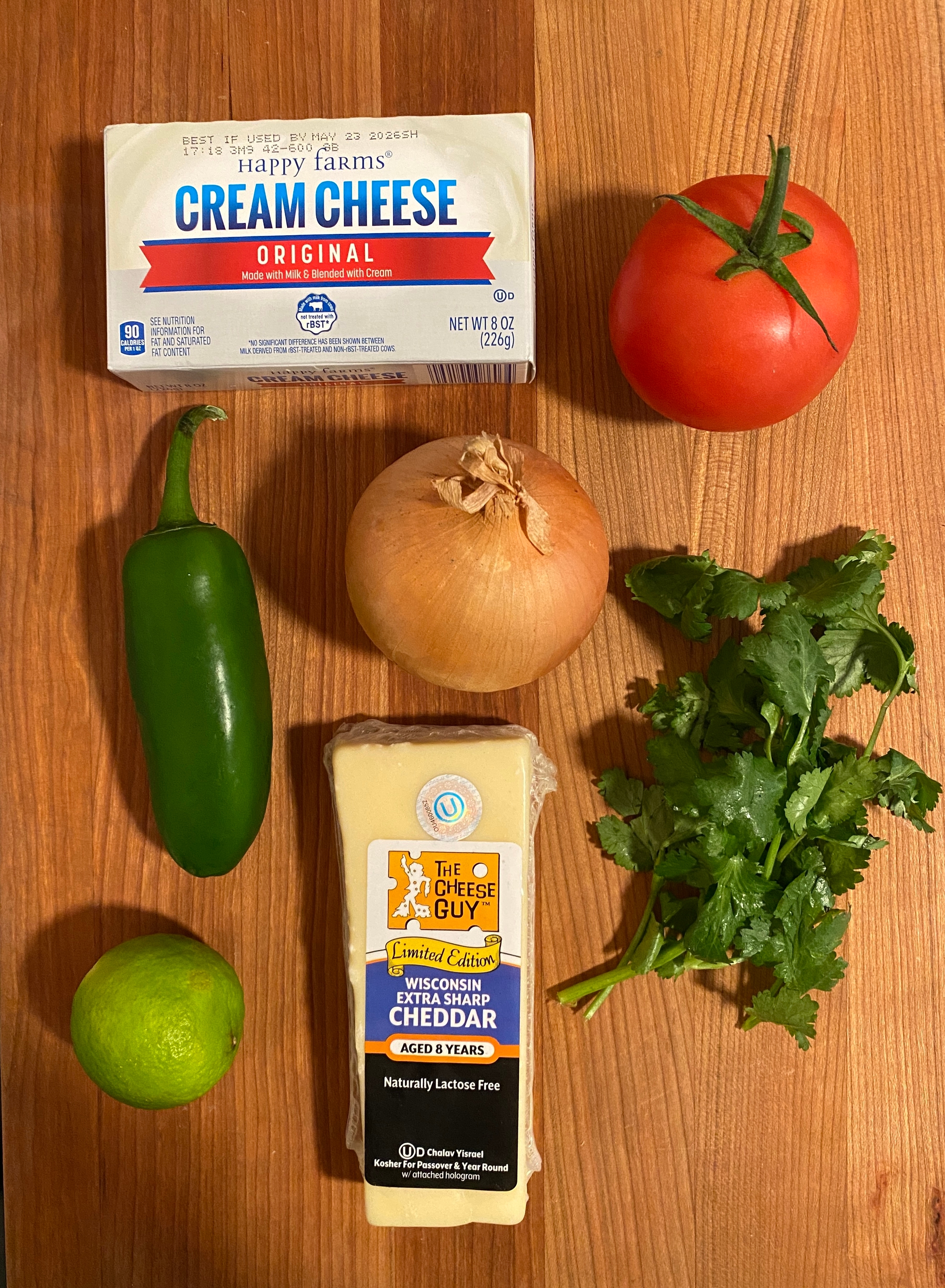 Cream cheese, tomato, onion, jalapeño, lime, cilantro, and aged cheddar on a wooden surface