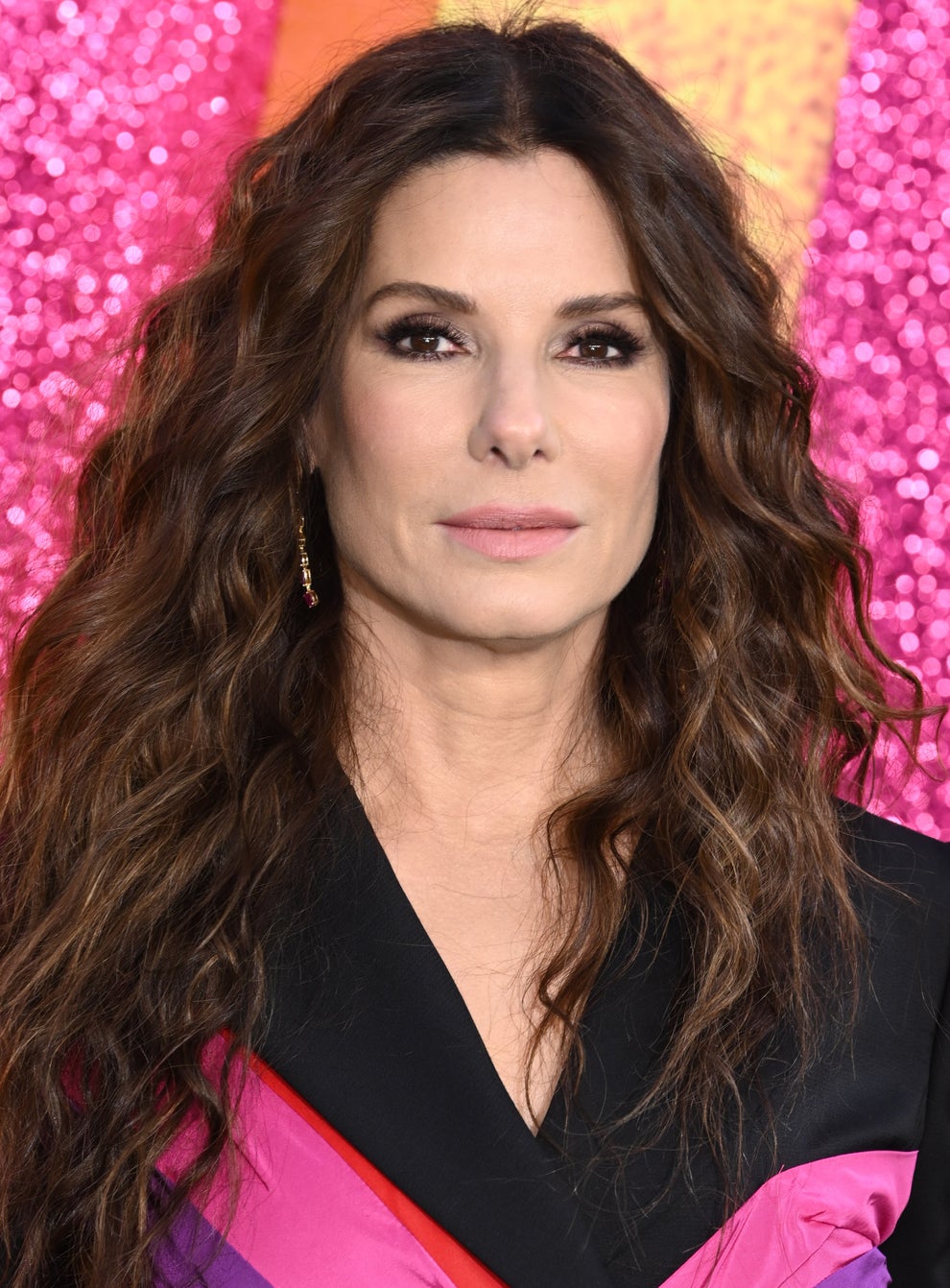 21 Jaw-Dropping "Then And Now" Photos Of Celebrities Who Have Gotten Wayyyyy Sexier With Age 68 A woman with long, wavy hair wears a black top with colorful accents, standing against a textured backdrop