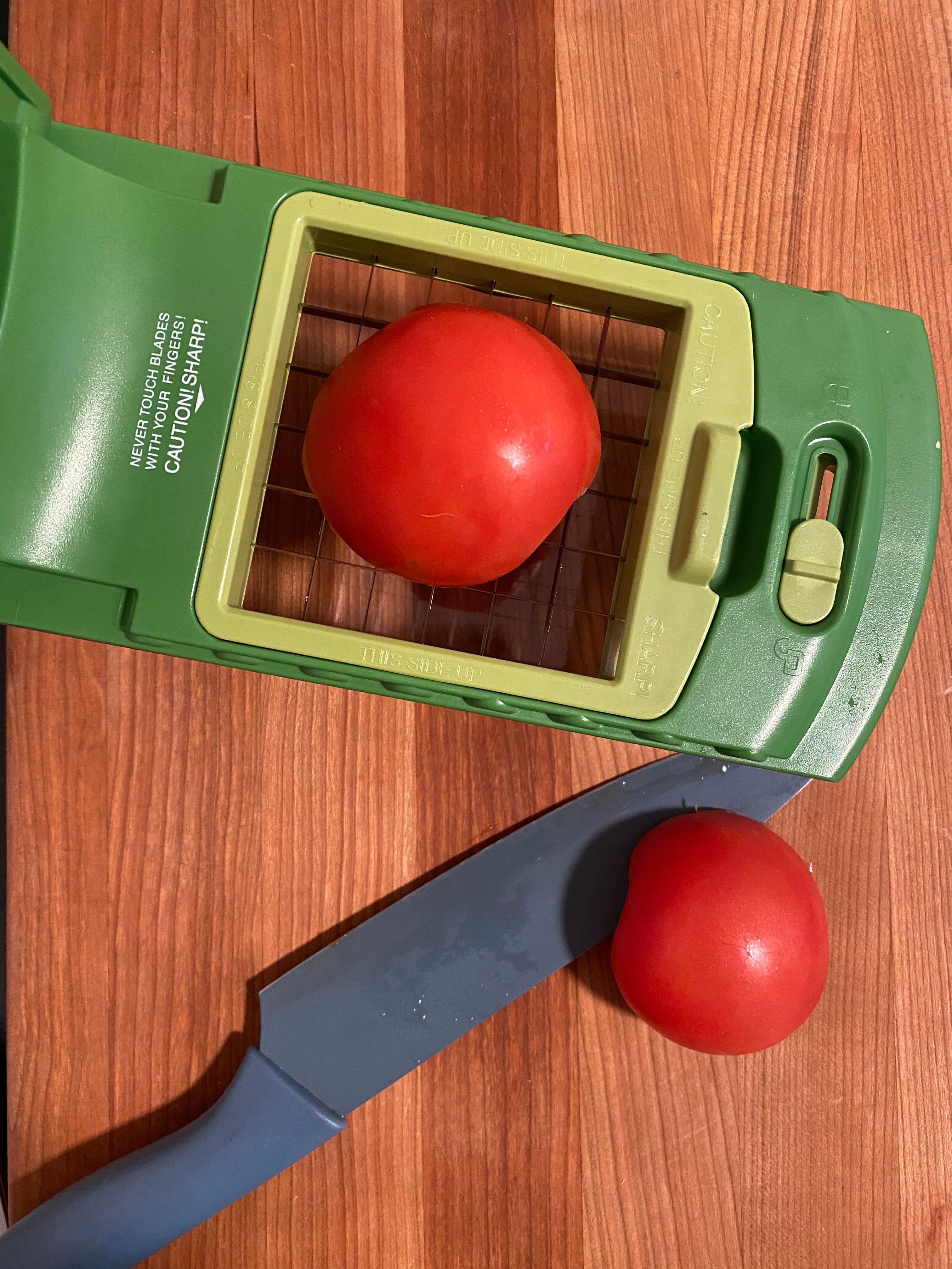 Half a tomato on a slicer with another half and a knife on a wooden surface