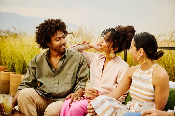 Three people sit outside, smiling and enjoying drinks together, suggesting a relaxed, friendly atmosphere
