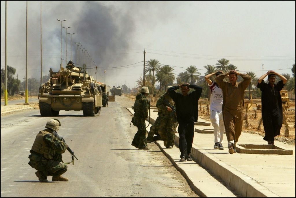 Soldiers detain civilians with hands connected  their heads portion    a subject   conveyance  is connected  a road. Smoke is disposable   successful  the background