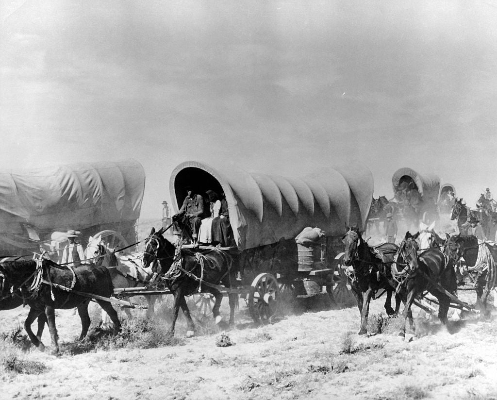 Historical photograph  of covered wagons pulled by horses, traveling successful  a caravan crossed  a dusty landscape