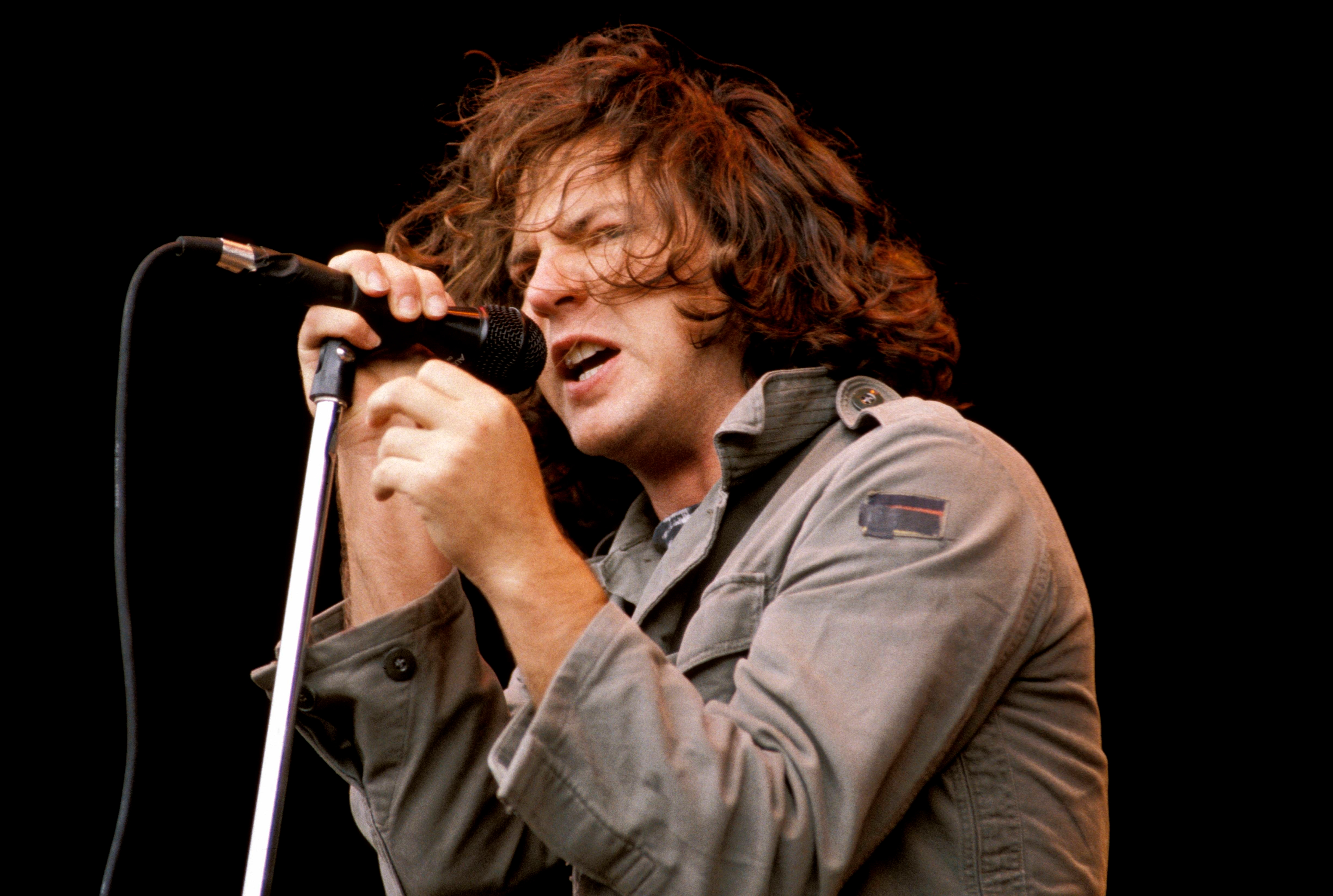 Singer passionately performing on stage, holding a microphone with both hands, wearing a casual jacket