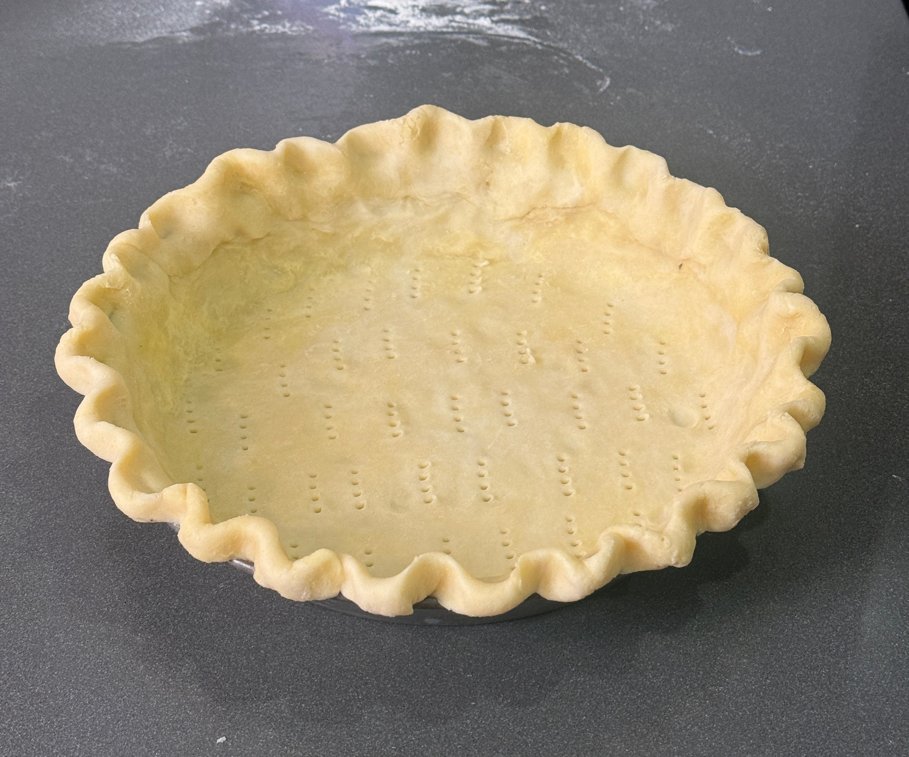 Unbaked pie crust with crimped edges in a dish, resting on a kitchen countertop