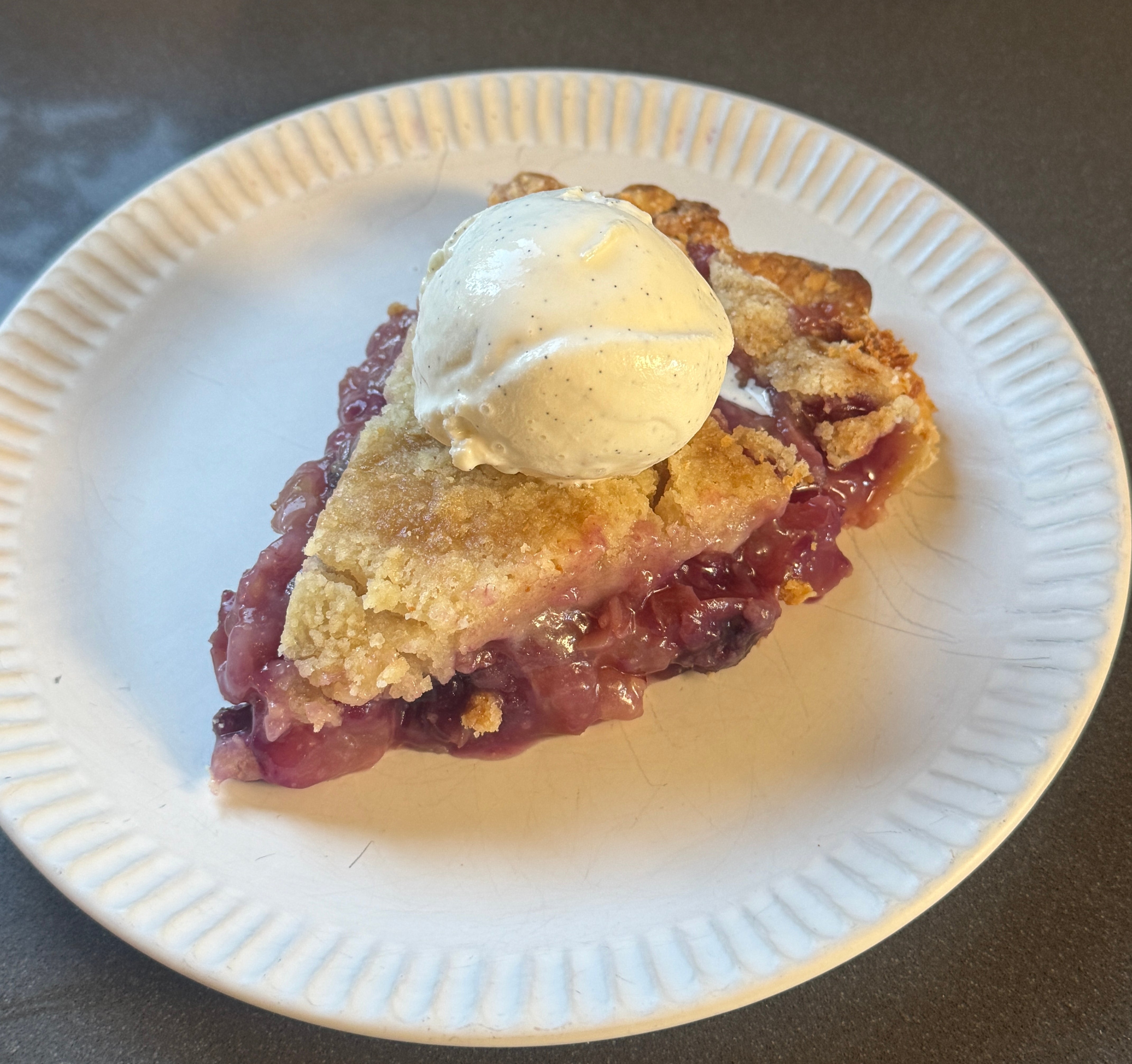 Slice of grape pie topped with a scoop of vanilla ice cream on a white plate