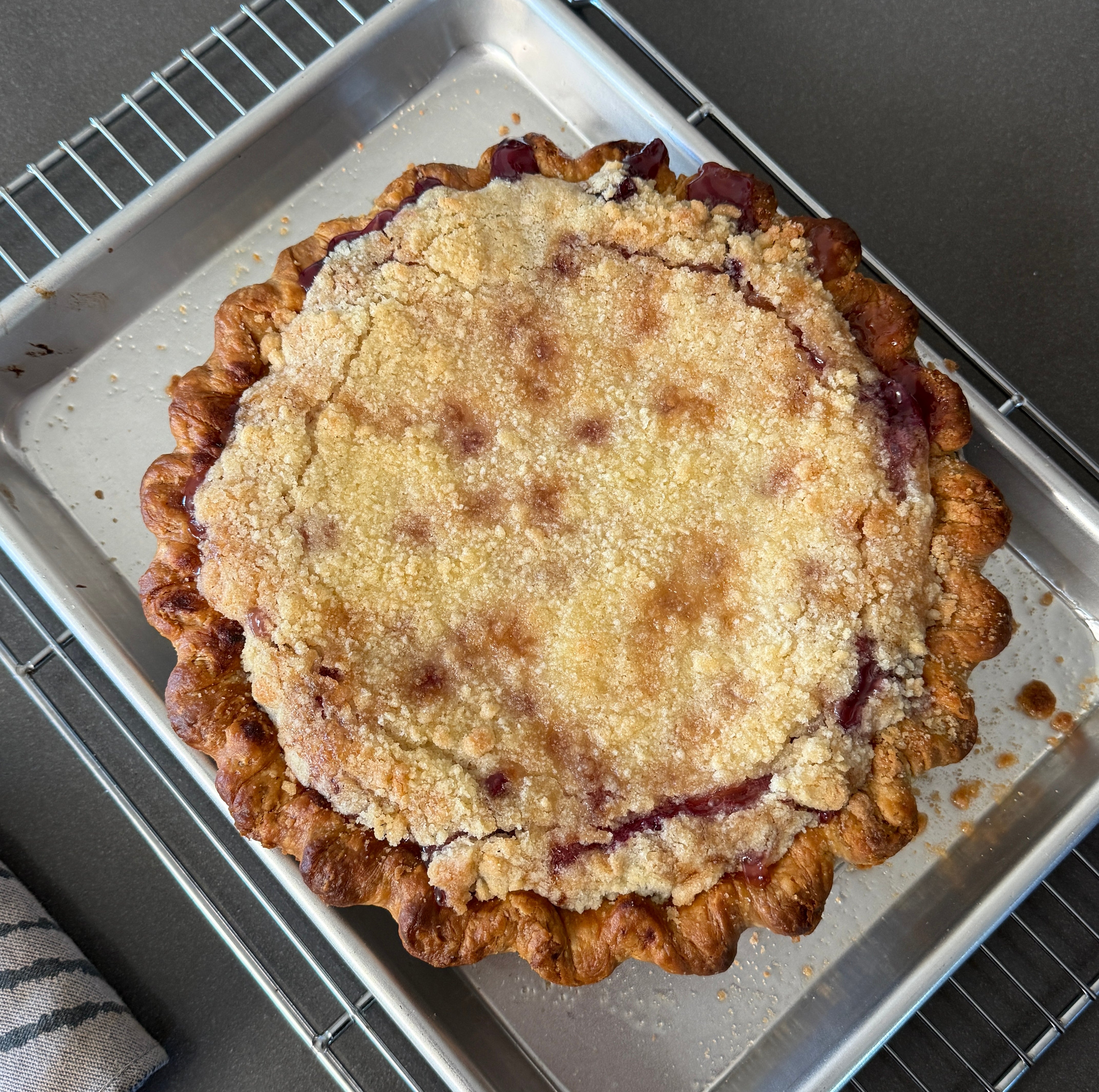 A freshly baked grape pie with a golden crust sits on a cooling rack, placed in a metal baking tray