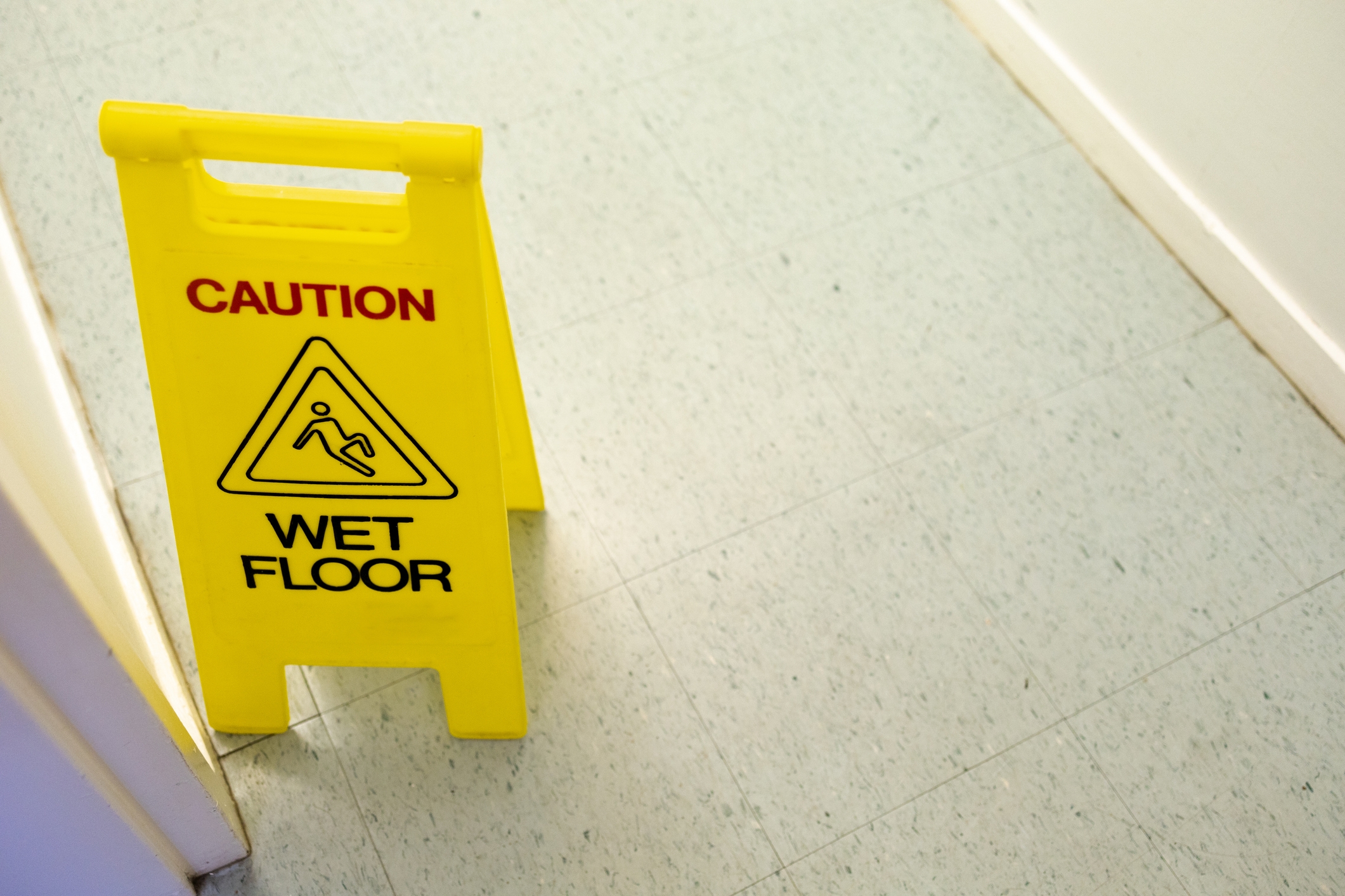 Yellow "Caution: Wet Floor" sign with a slipping figure on a tiled floor