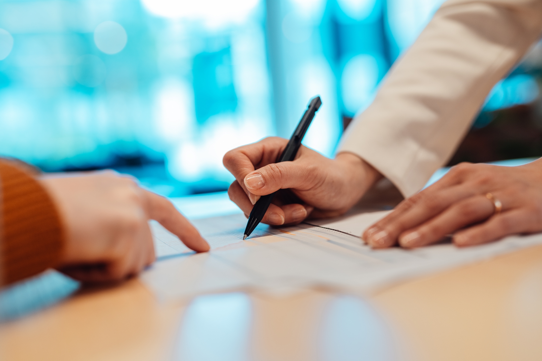 Hands signing a document on a table, indicating a business agreement or financial transaction