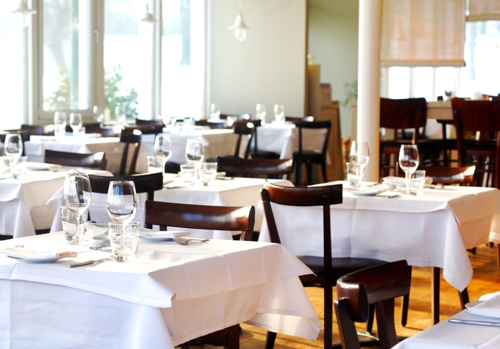 Restaurant interior with neatly arranged tables set for dining, with white tablecloths and glassware, ready for service