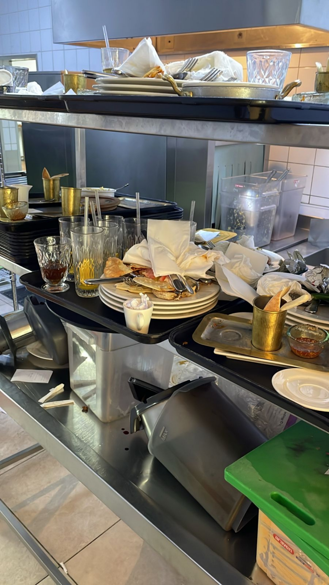 Messy kitchen sink area filled with used plates, glasses, and utensils, suggesting a busy restaurant environment and workload