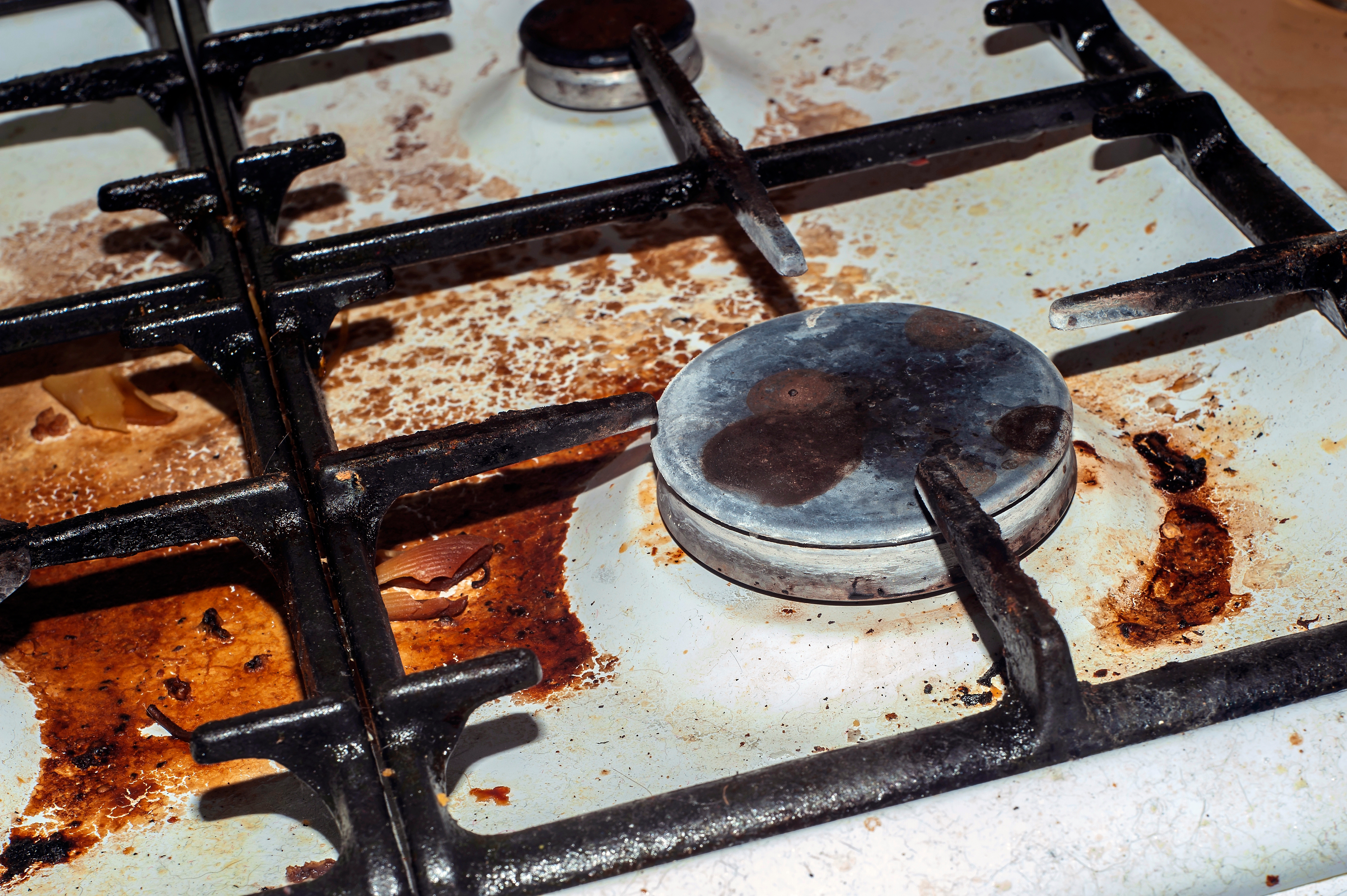Farget komfyrtopp med fastbrent søl og smuss rundt brennerne, noe som indikerer mye bruk og mangel på rengjøring