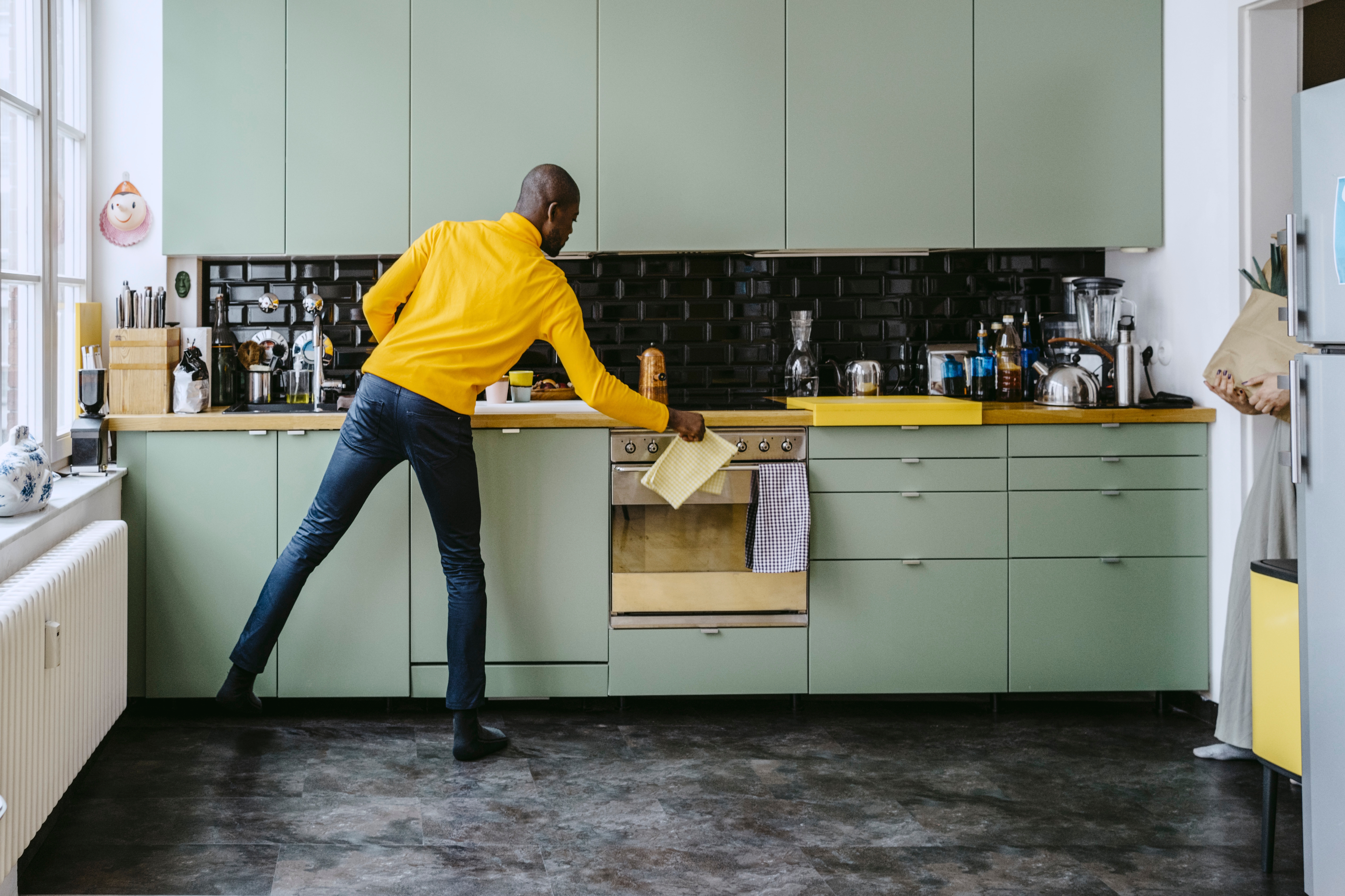 Mann på et kjøkken som strekker seg etter et papir på benken, omgitt av forskjellige kjøkkenartikler og apparater