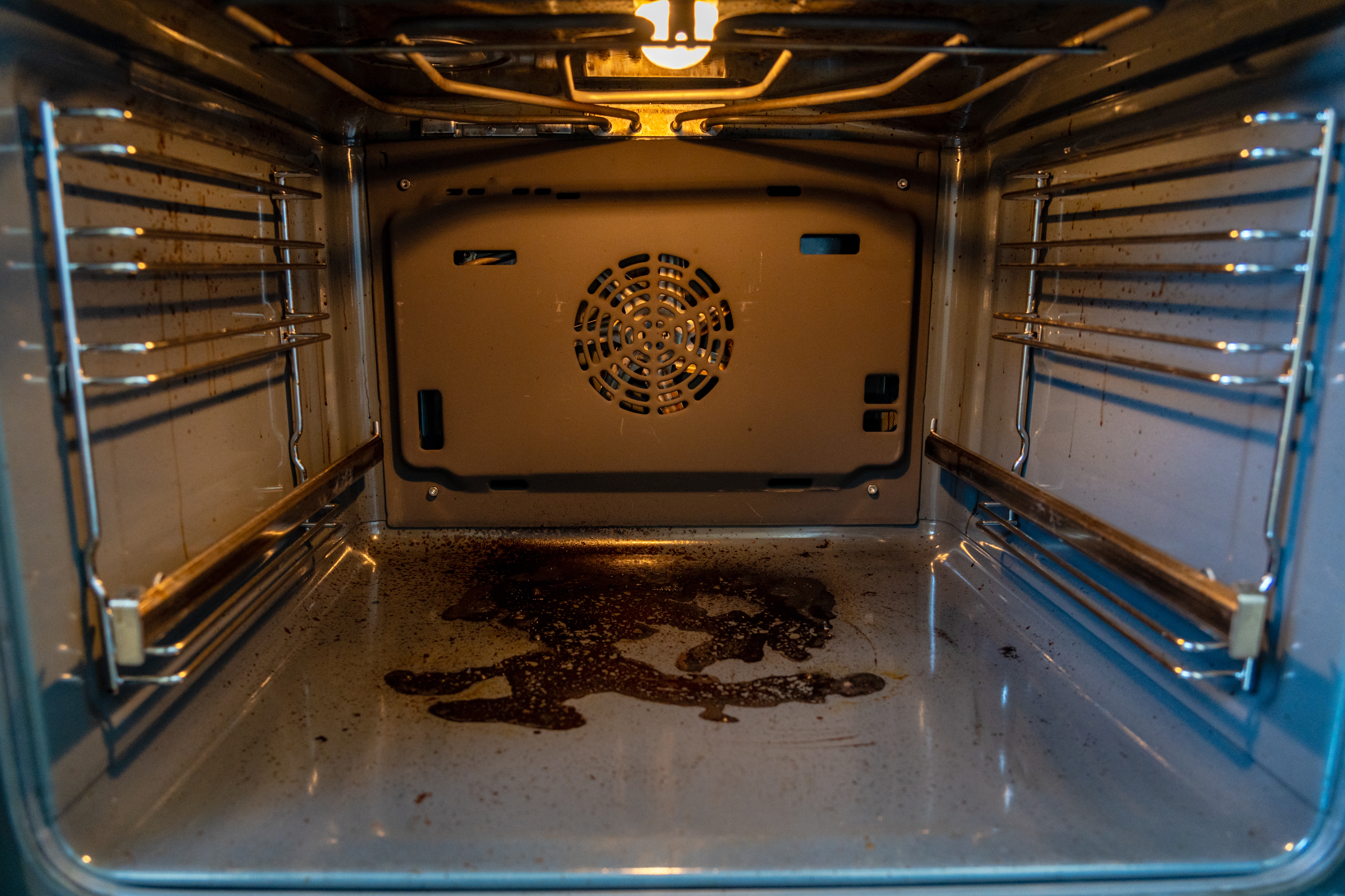 Skitten ovnsinteriør med fett og matflekker på bunnen. Ovnslyset er på, og fremhever rotet