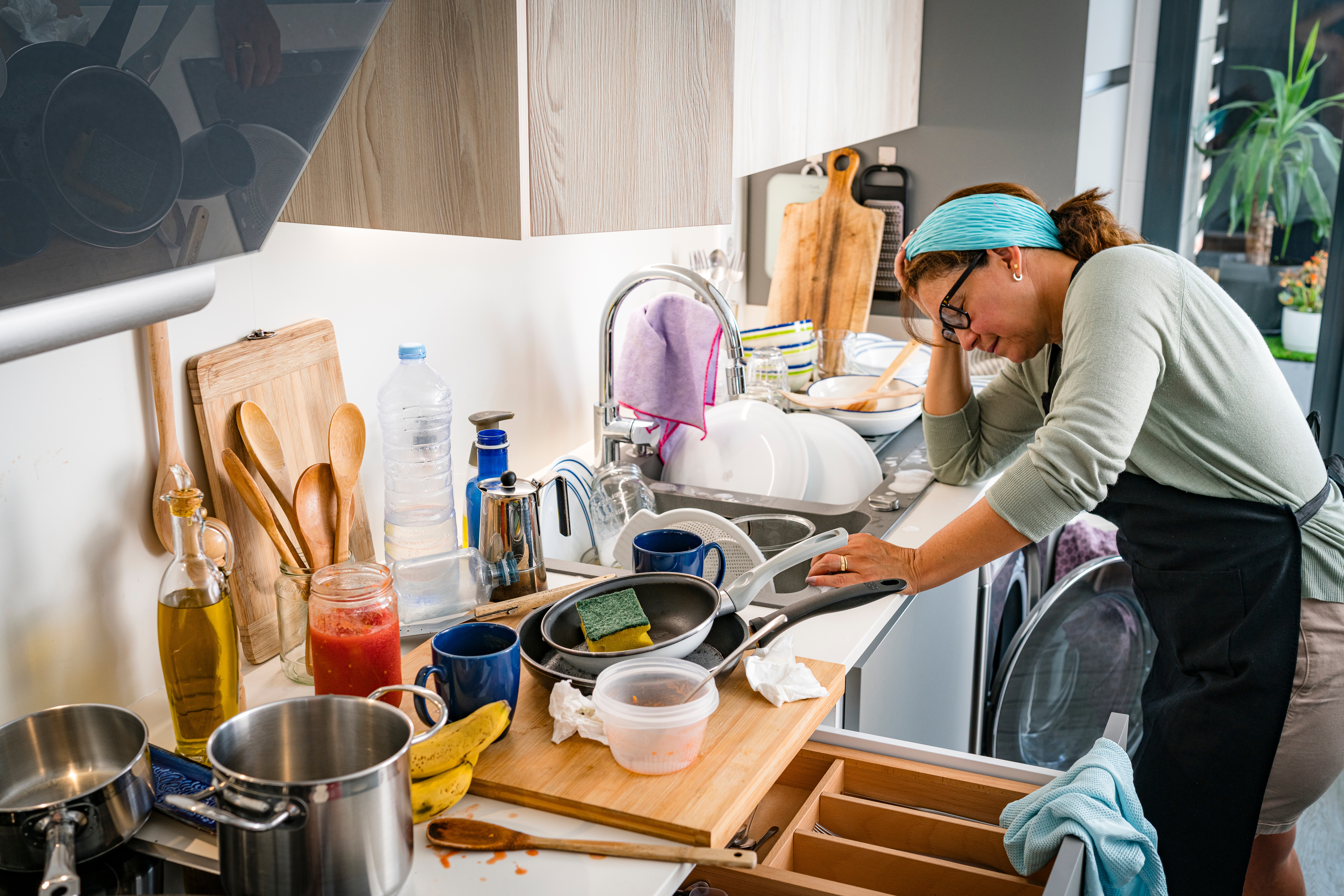 Person på et kjøkken, omgitt av skitten servise og kjøkkenutstyr, ser overveldet ut og sjekker en enhet