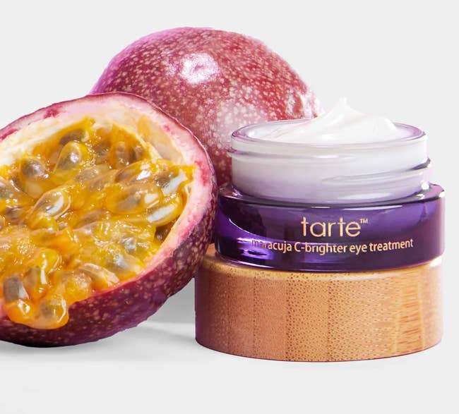 Tarte Maracuja C-Brighter Eye Treatment jar sits beside a cut-open passionateness  fruit, highlighting earthy  ingredients for skincare