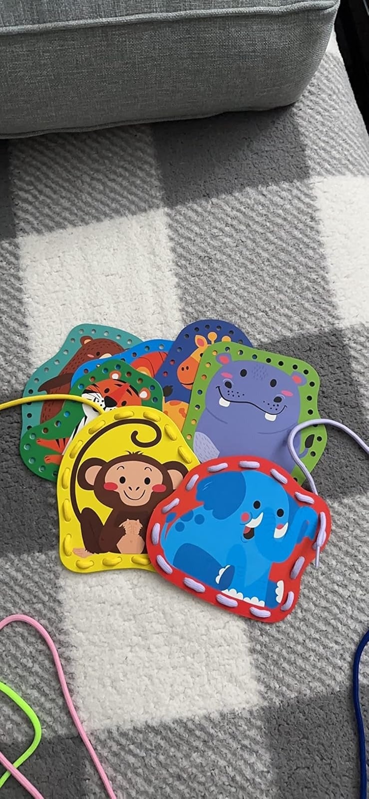 Colorful animal-themed lacing cards, featuring a monkey, elephant, and more, arranged connected  a checkered surface. Suitable for children's activities