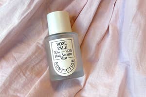 テキスト「ROSE PALE Hair Serum Mist 30ml - 1.0fl. oz NONFICTION」のボトルが布の上に置かれています。