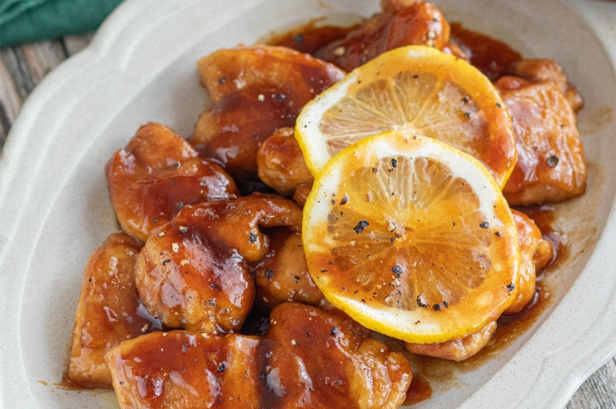お皿に盛られたレモンスライス付きのチキン料理。タレがかかっており、箸が置かれている。