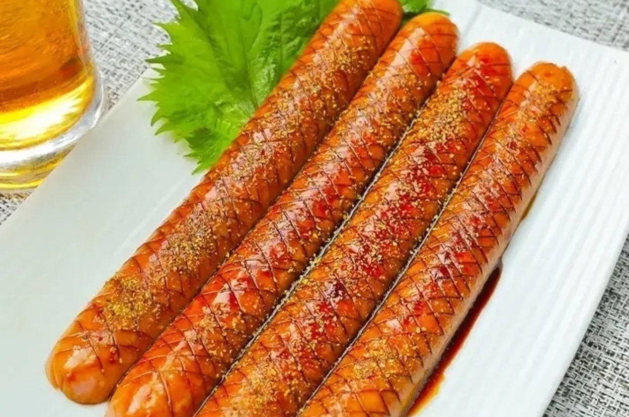 お皿に盛り付けられた調味料がかかったソーセージ4本とシソの葉。隣に飲み物がある。