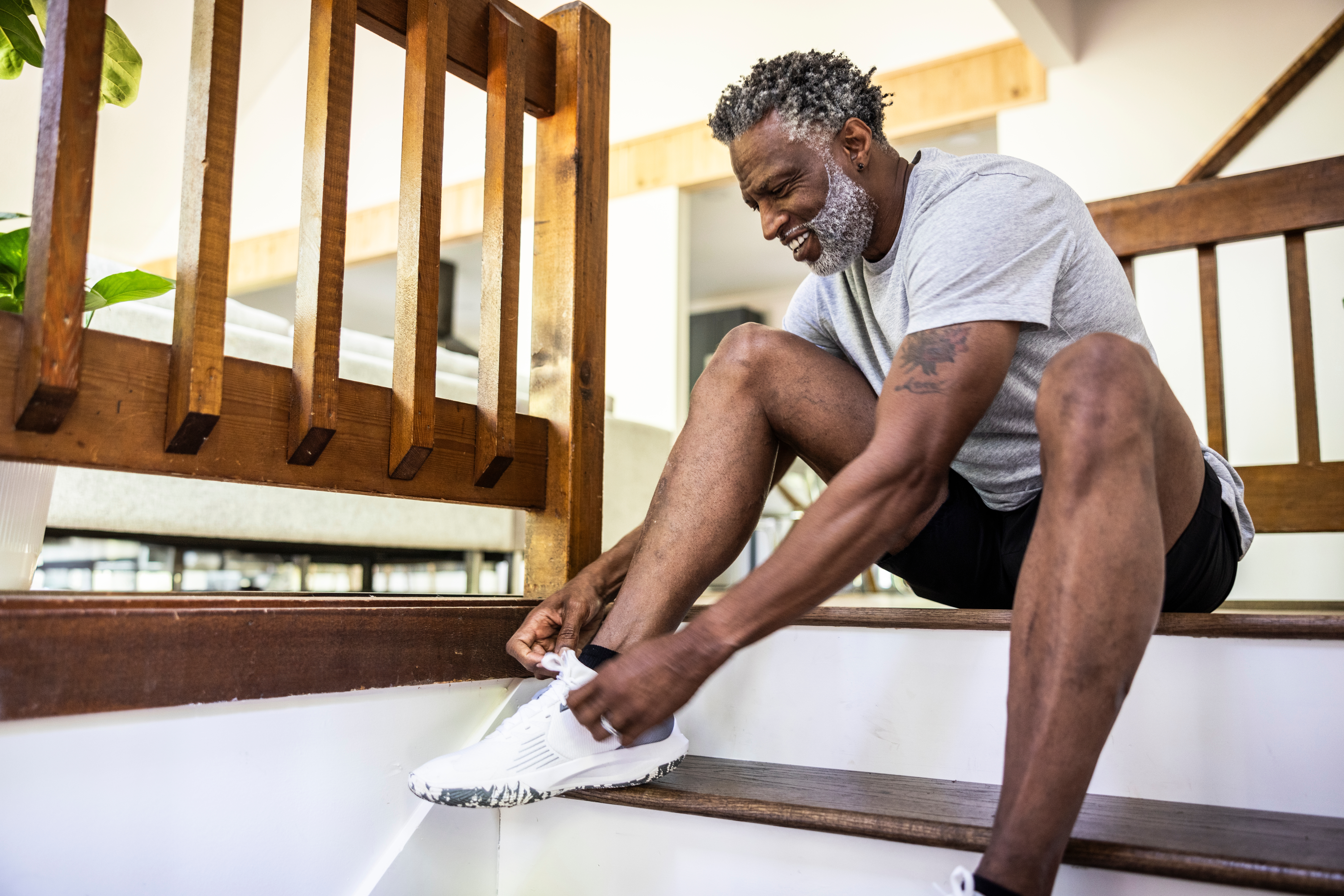 Mann i atletisk tøy sitter på trapper, knytter joggeskoen med et smil, noe som tyder på avslappet og uformell morgenberedskap