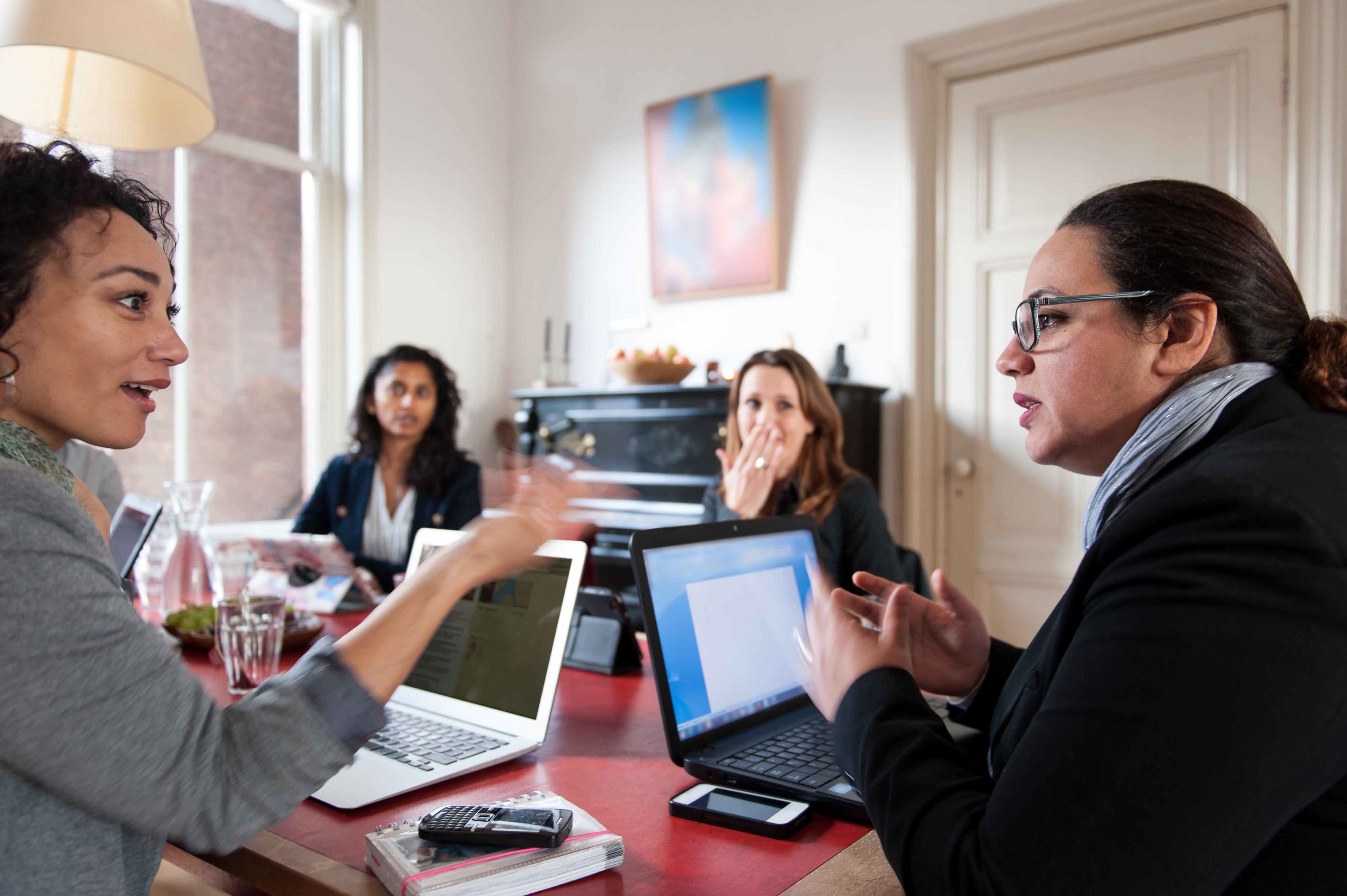 Fire personer i forretningsantrekk har en diskusjon rundt et bord med åpne bærbare datamaskiner i et kontormiljø