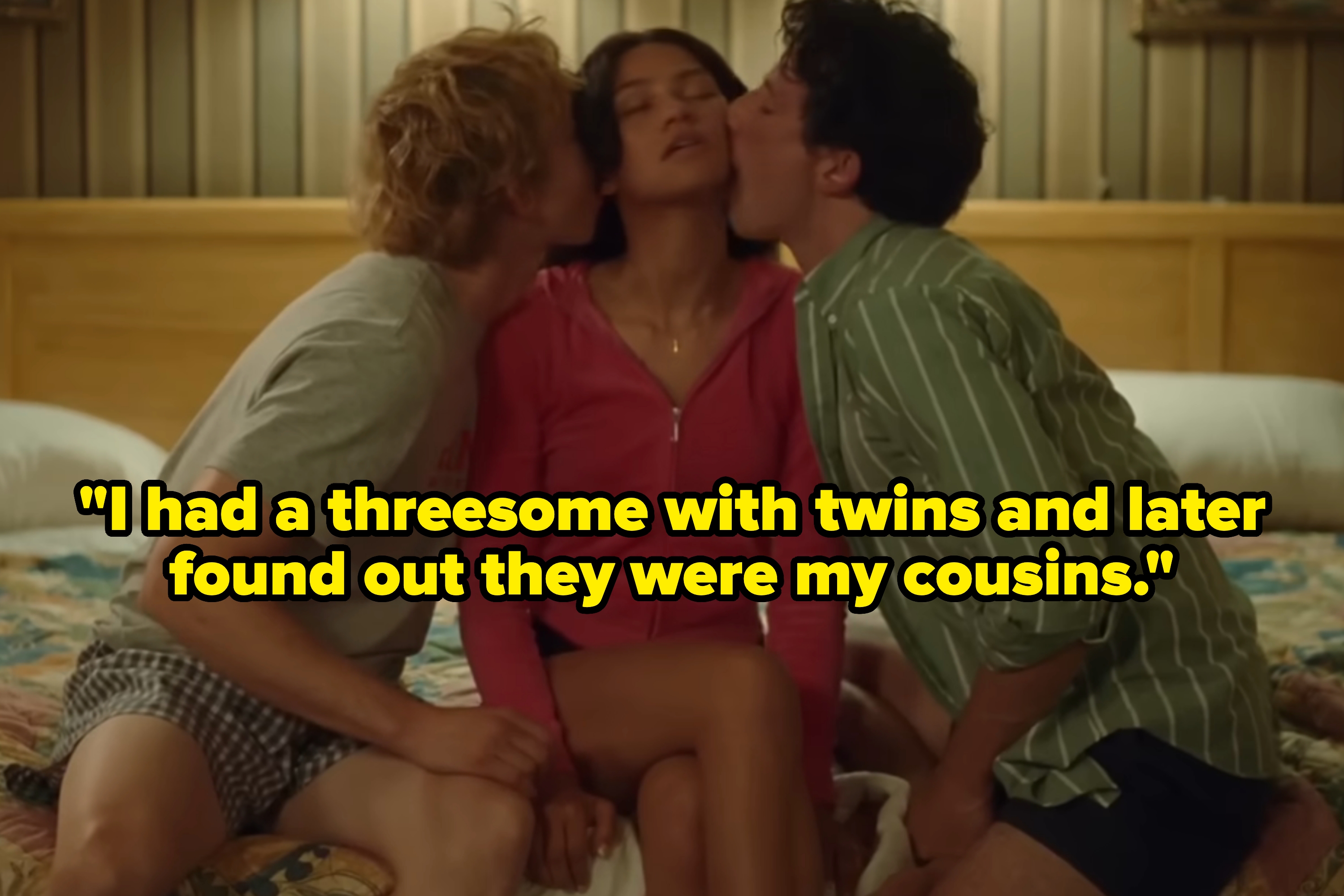 Three people sitting on a bed; person in the middle is kissed on both cheeks, wearing casual attire, suggesting intimacy