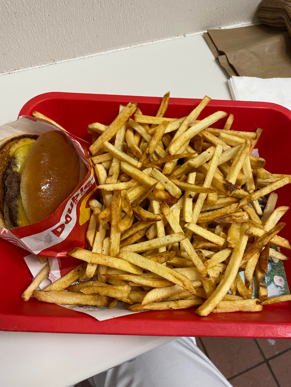 A tray with a cheeseburger partially wrapped and a large serving of fries. Napkin and paper bag visible in the background