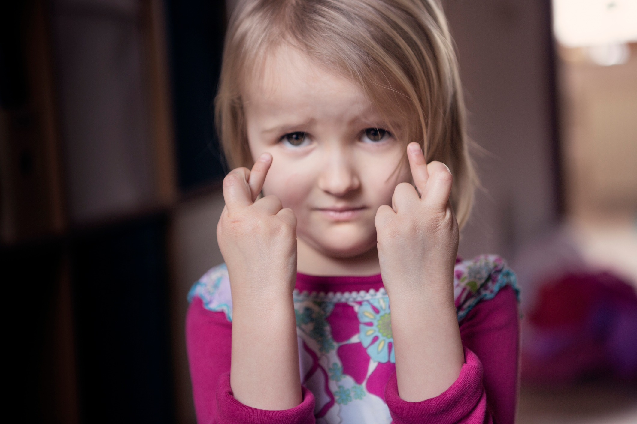Barn med et alvorlig uttrykk holder opp begge langfingrene, iført en blomstermønstret kjole