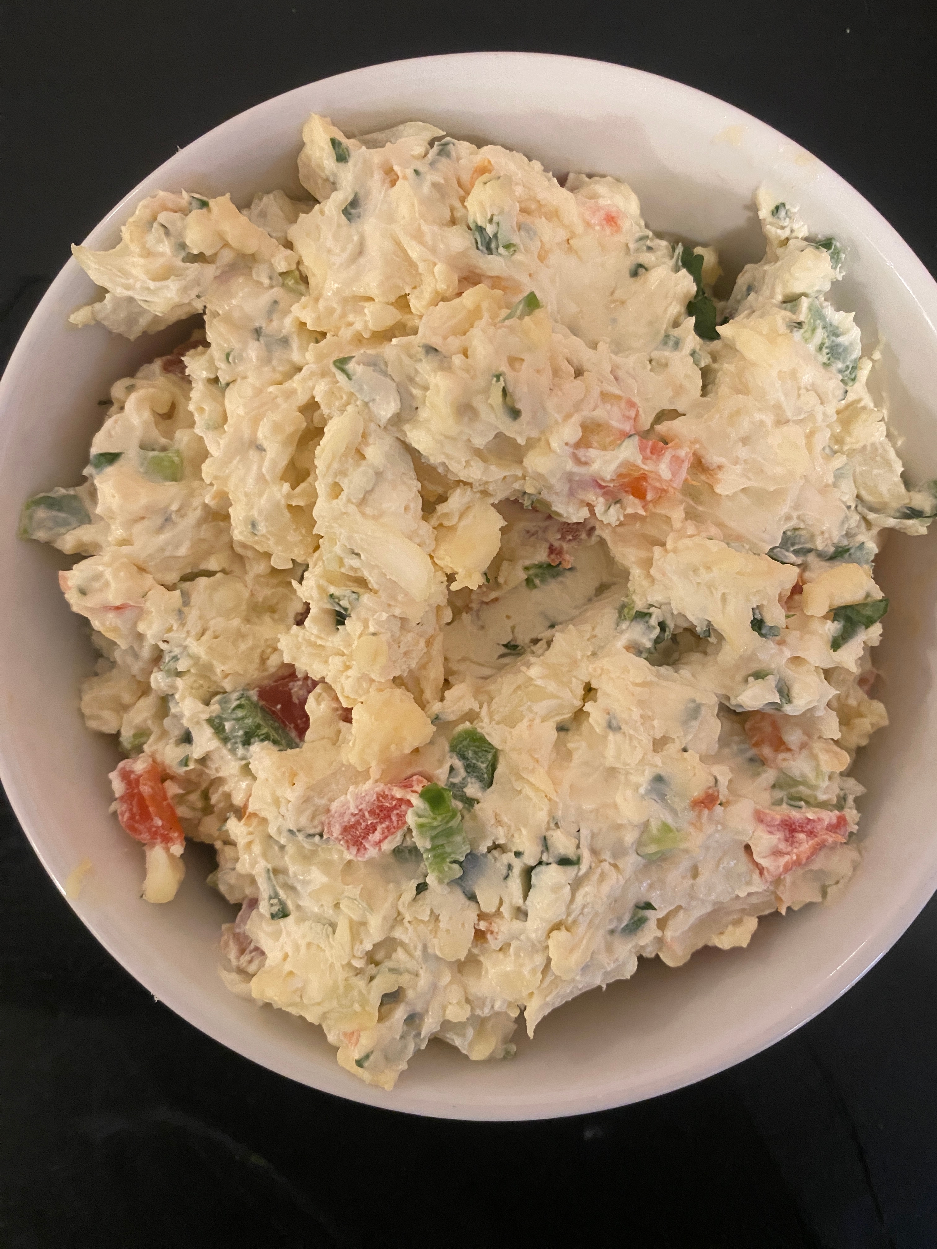 A bowl of creamy-looking potato salad with chopped vegetables mixed in
