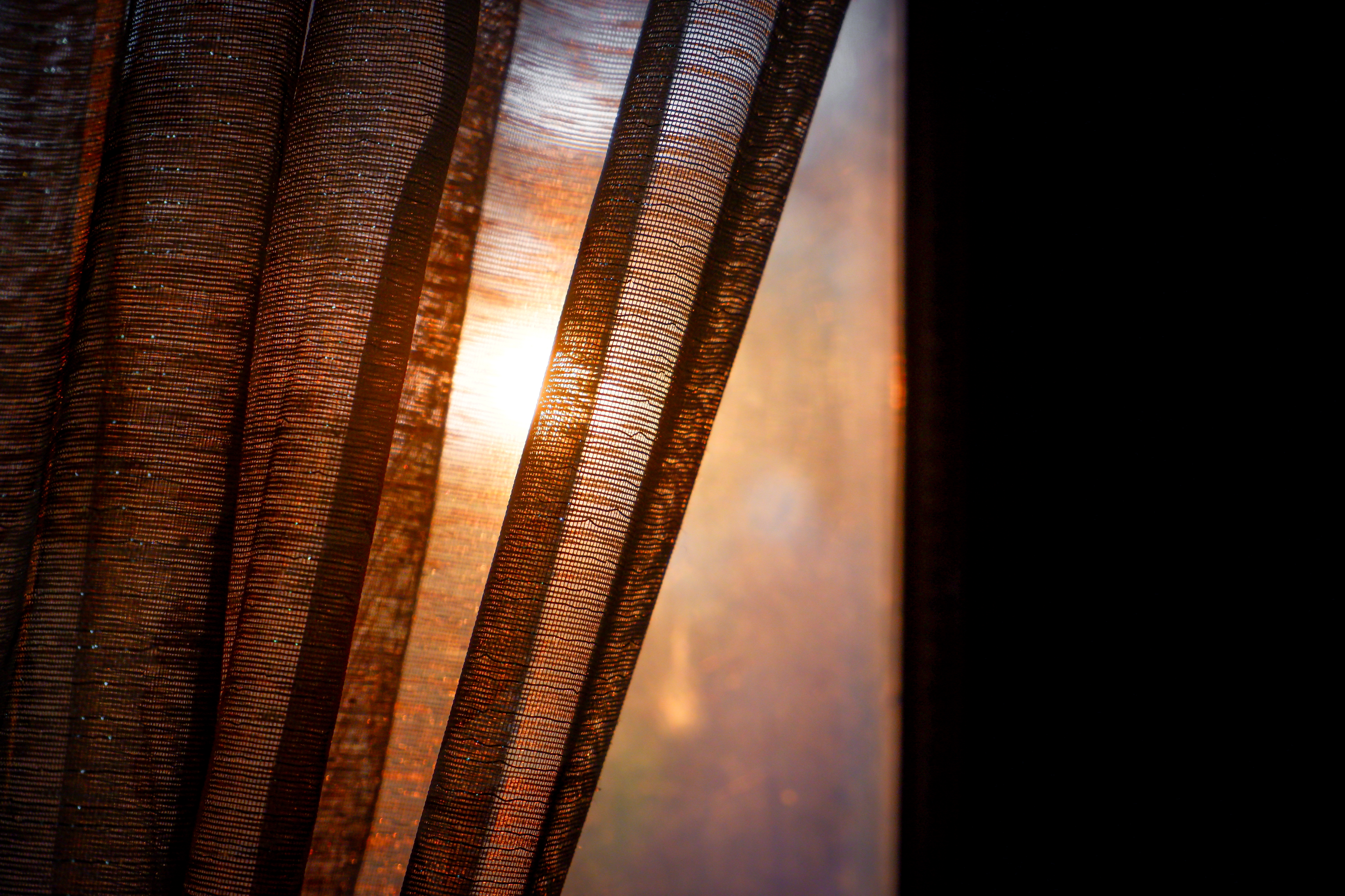 Sollyset titter gjennom delvis åpne, teksturerte gardiner og skaper en varm og rolig atmosfære