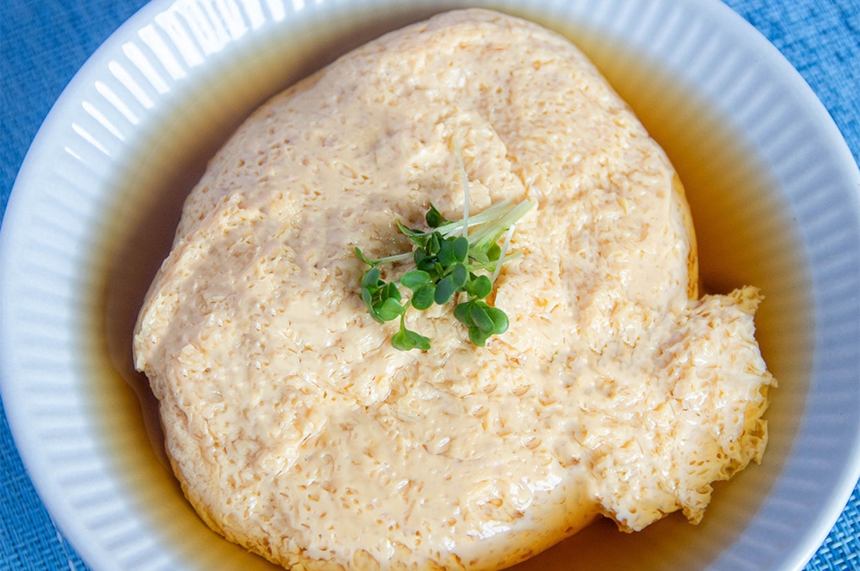 丸い白い皿に盛られた卵豆腐の上に、小さな緑の葉がのっている。