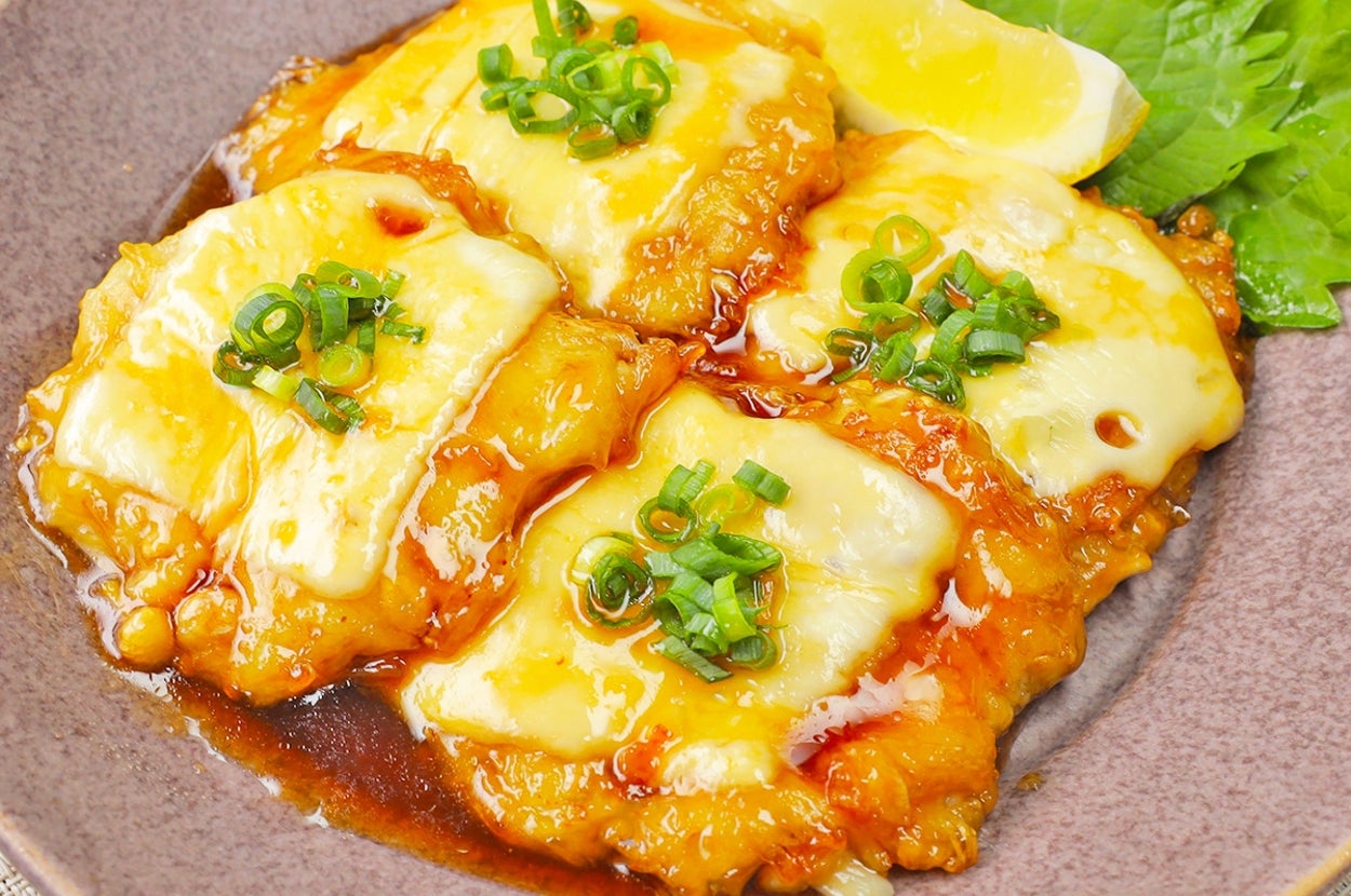 チーズとねぎをトッピングした照り焼きチキンが皿に盛られている。付け合わせにレモンと緑葉あり。