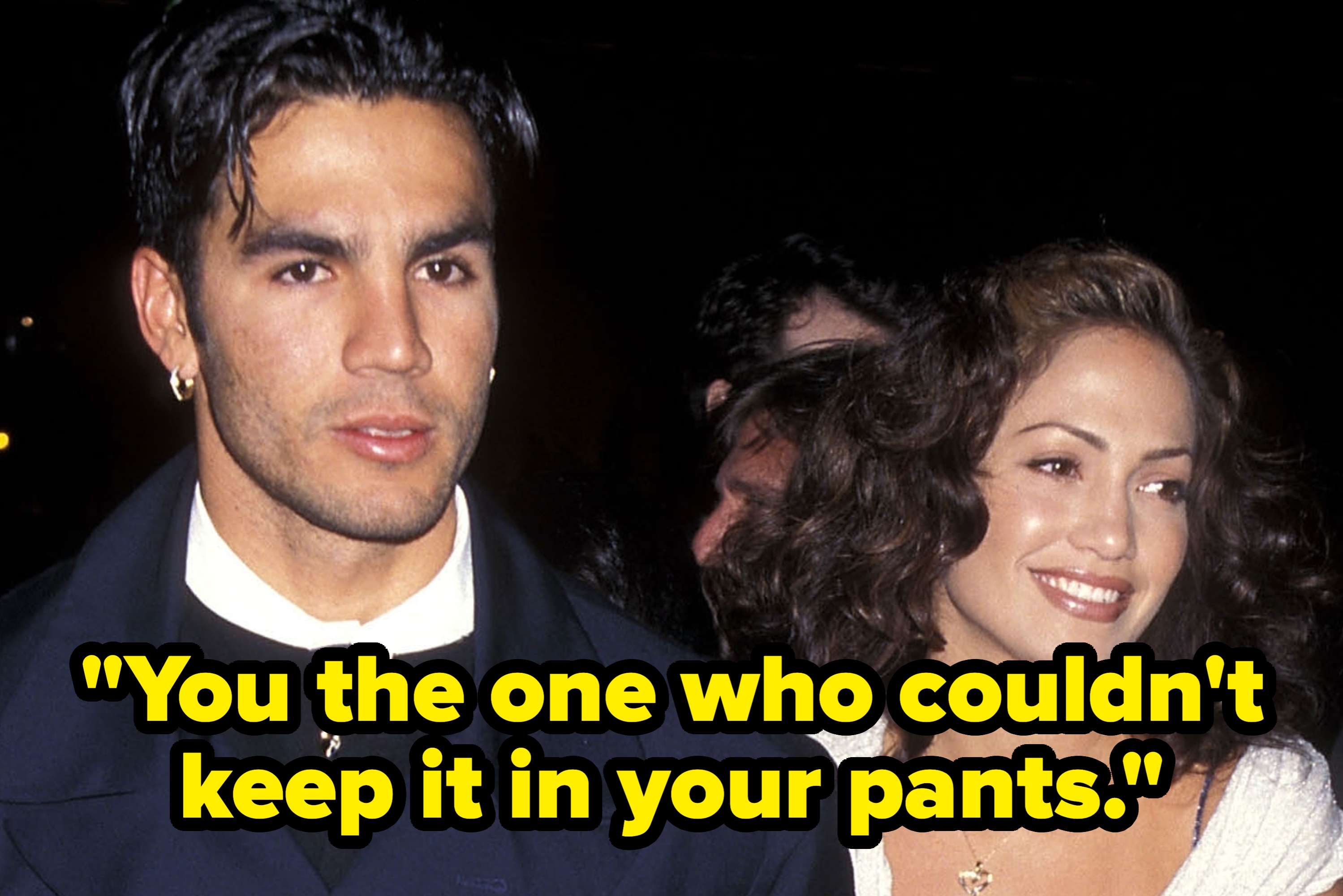 Two people on the red carpet; one wears a formal suit, the other a sleeveless, knee-length dress with a draped shawl, smiling and walking