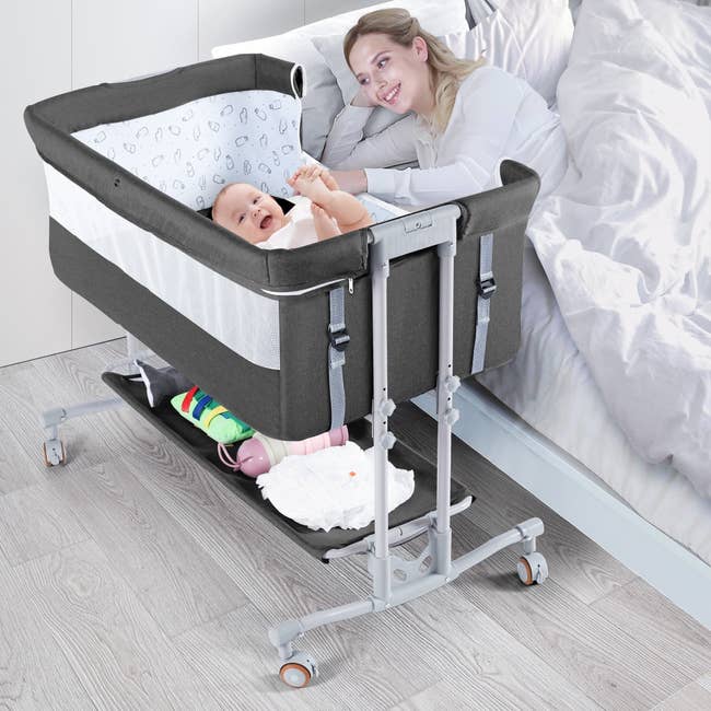 A idiosyncratic lies successful furniture smiling astatine a babe successful a bedside bassinet with attached storage