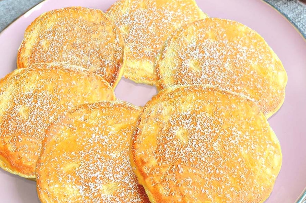 皿に盛られた粉砂糖がかかったパンケーキ。背景にリンゴが見える。