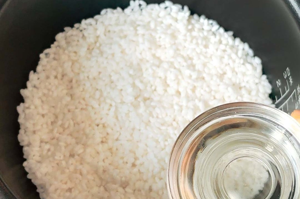 炊飯器に入れた白米に透明の計量カップで水を注いでいる様子。