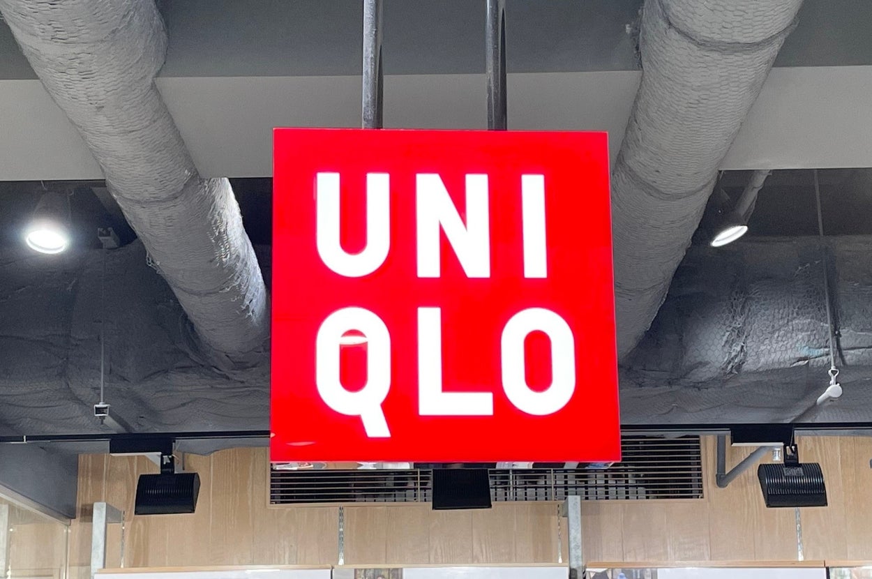 Sign reading "UNIQLO" hangs from a ceiling with exposed ducts in a retail setting