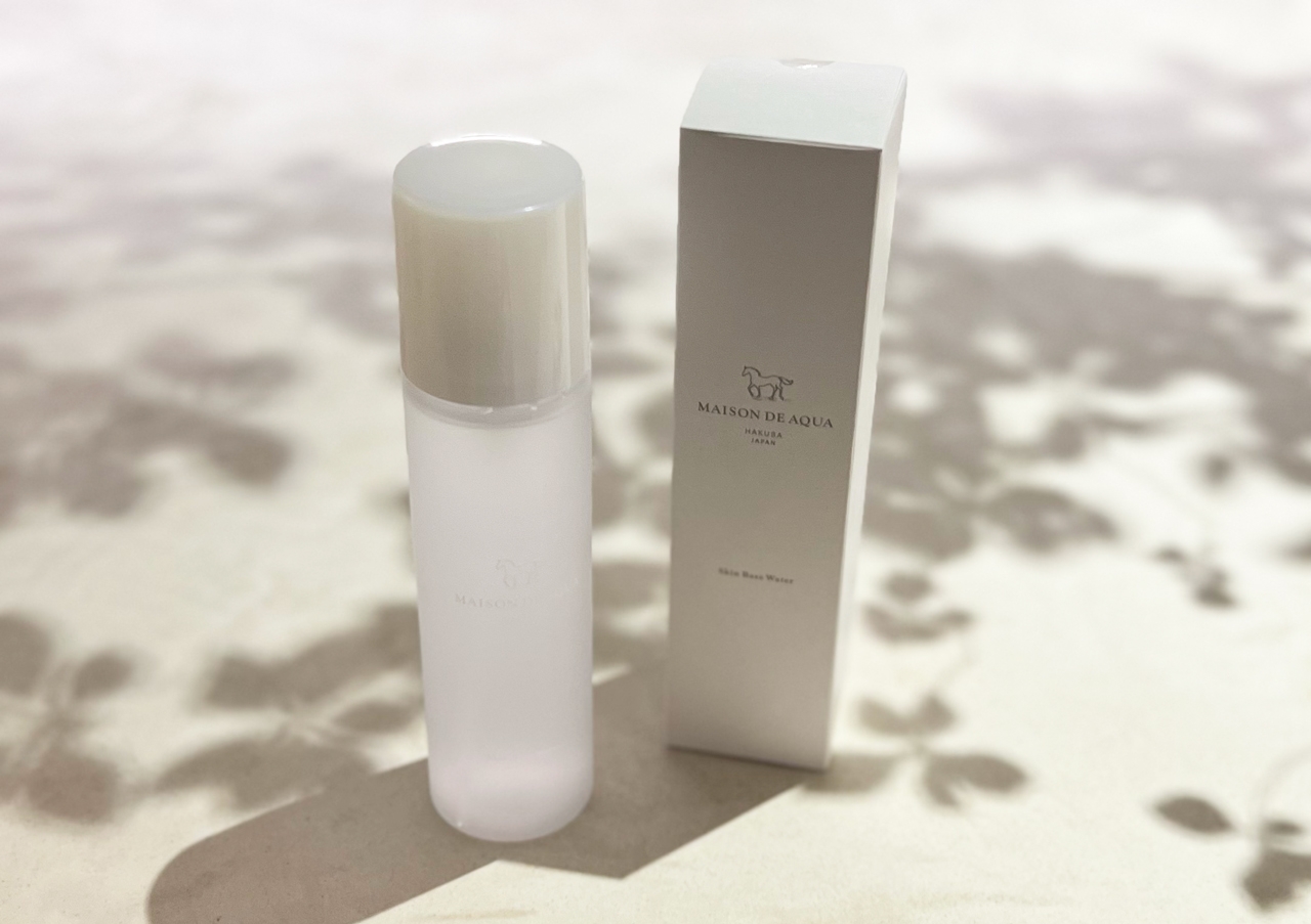 Skincare bottle and its box on a soft, shadowed surface. The bottle is minimalistic, with a sleek design. The brand logo is visible on the box