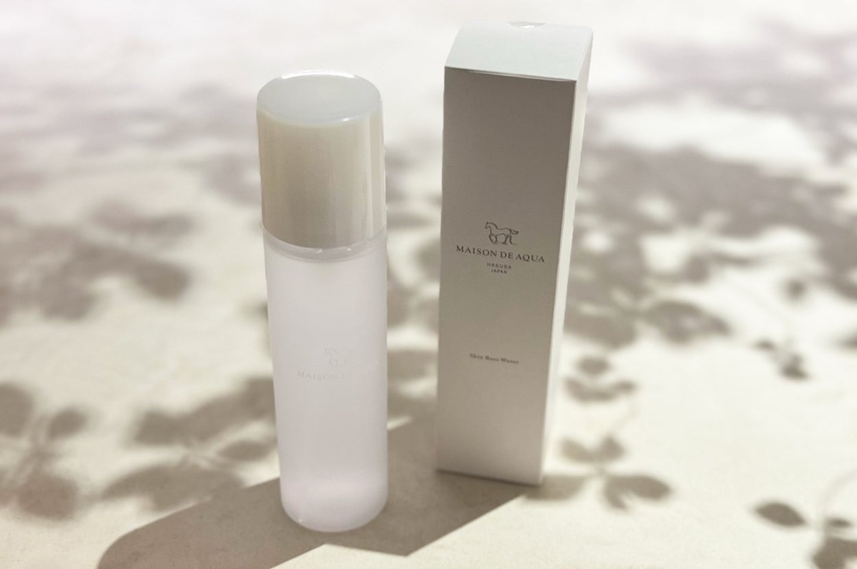 Skincare bottle and its box on a soft, shadowed surface. The bottle is minimalistic, with a sleek design. The brand logo is visible on the box