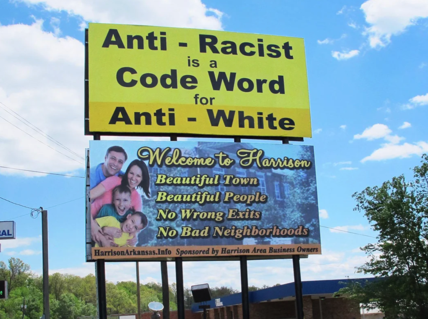 A billboard in a rural area reads "Anti-Racist is a Code Word for Anti-White." Text below welcomes people to a nearby town