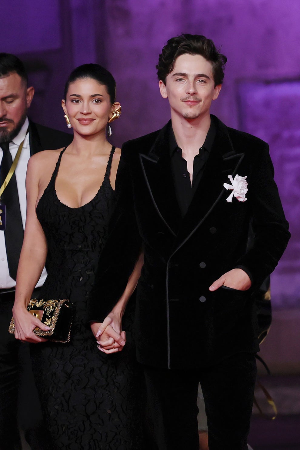 14 Celeb Feuds That Were SO One-Sided, They Were Basically Beefing With A Brick Wall 76 Two individuals hold hands on a red carpet. The woman wears a detailed black dress and the man sports a tailored black velvet suit with a floral pin