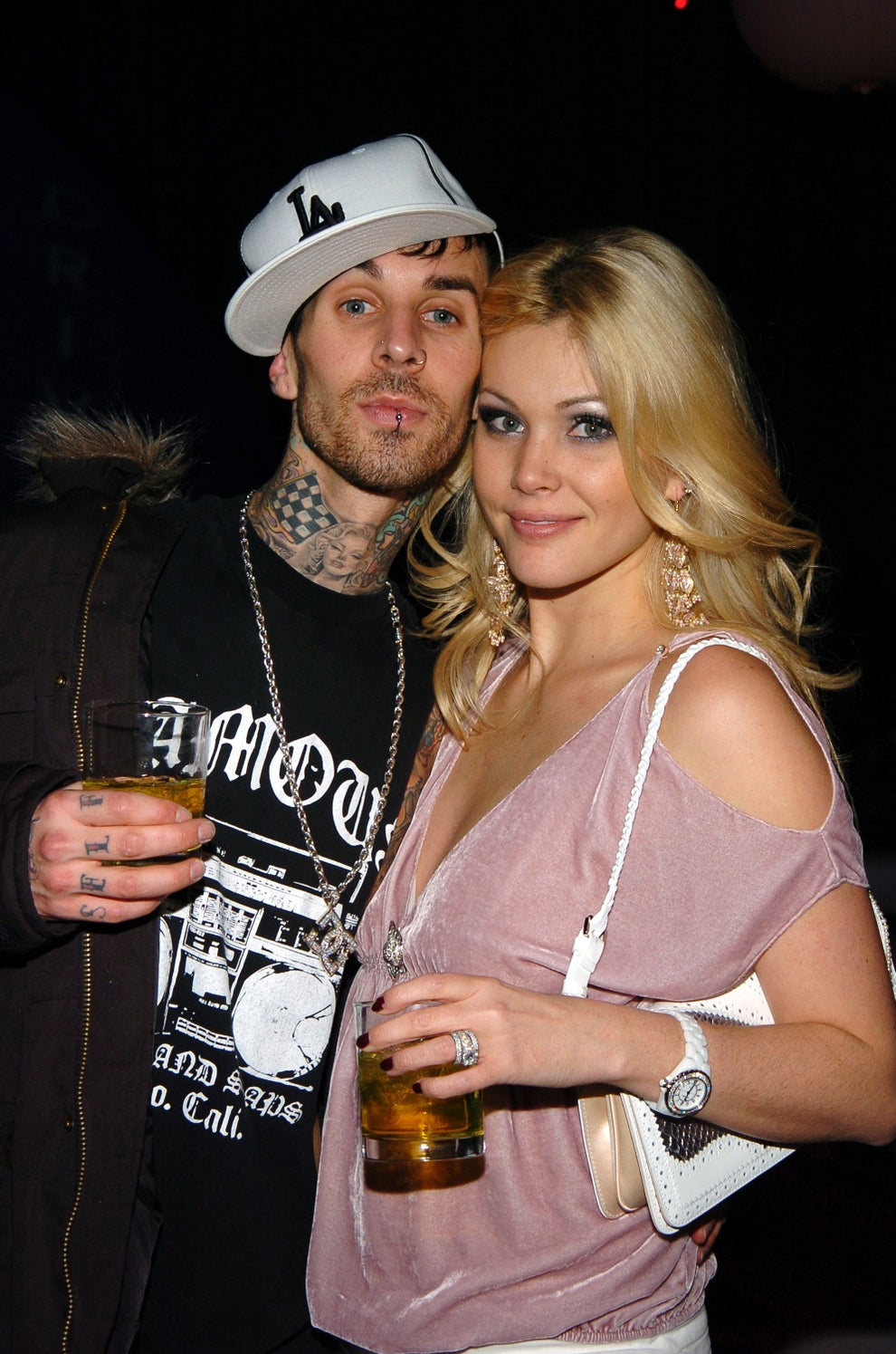 14 Celeb Feuds That Were SO One-Sided, They Were Basically Beefing With A Brick Wall 64 Two people pose together holding drinks. The man wears a casual outfit with a cap, and the woman wears a dress with a shoulder bag and long earrings
