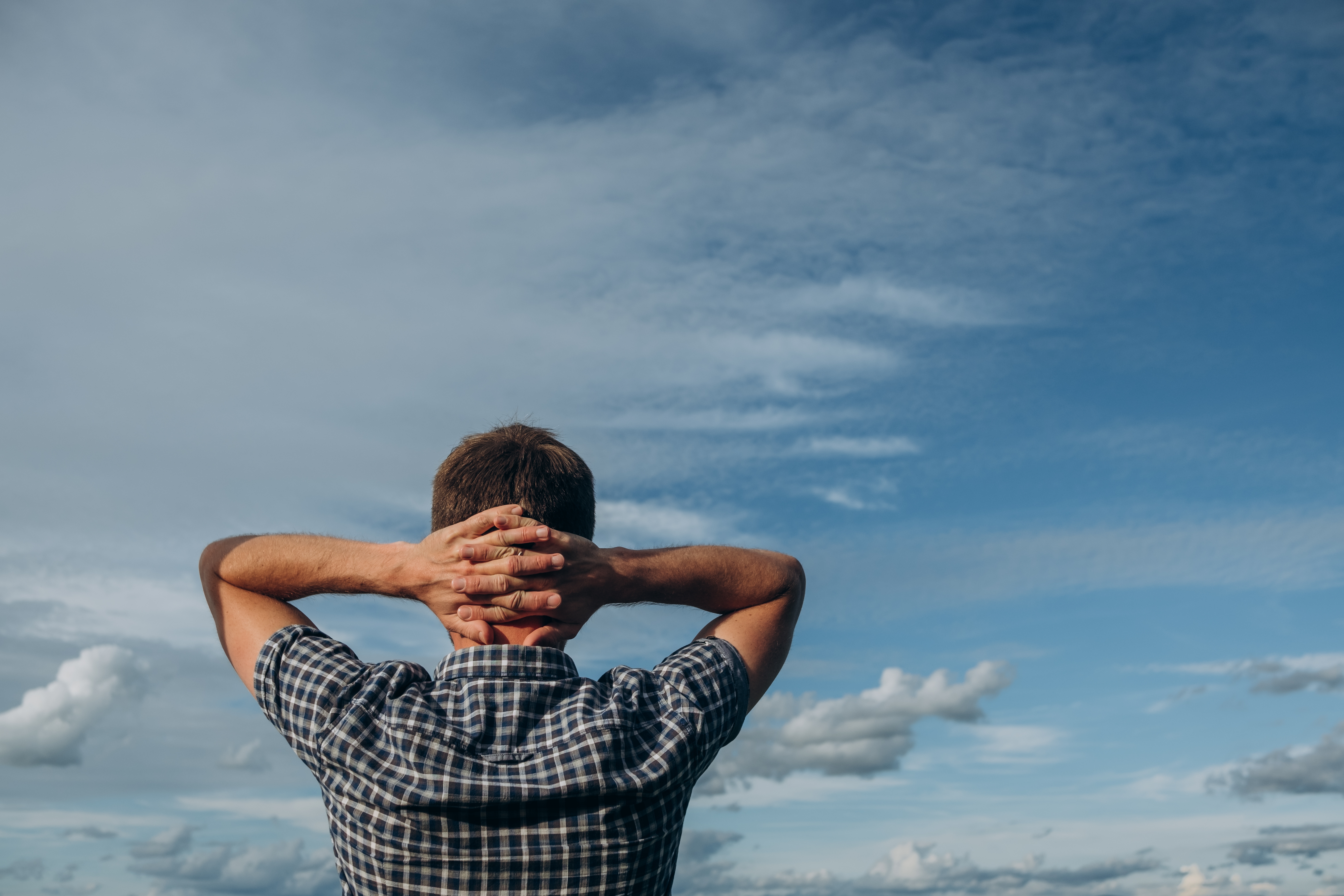 Person i rutete skjorte med hendene bak hodet, ser på åpen himmel