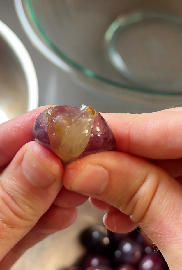 Hands peeling a grape with precision, revealing its translucent interior
