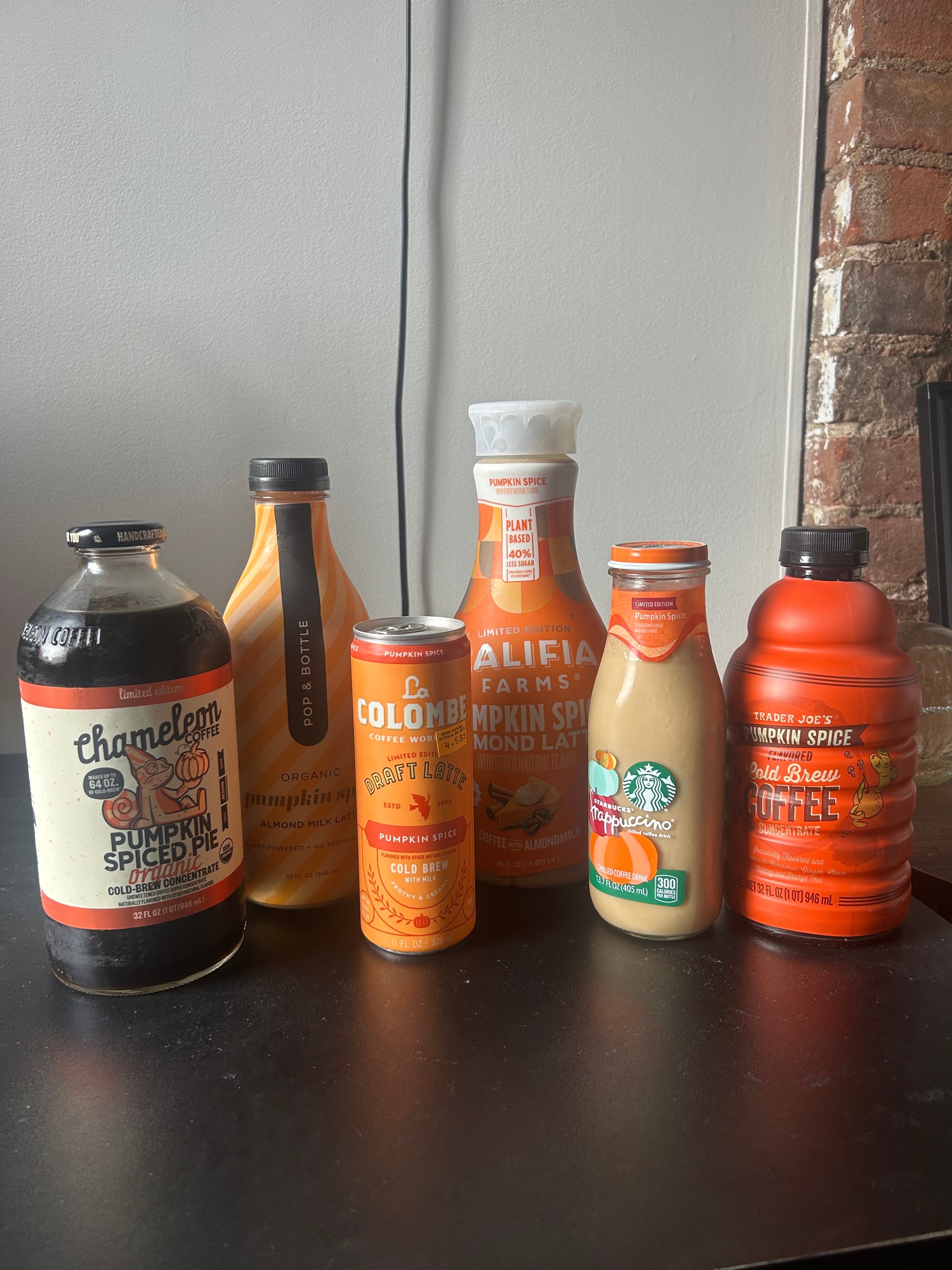 A variety of pumpkin spice coffee beverages from different brands are displayed on a table