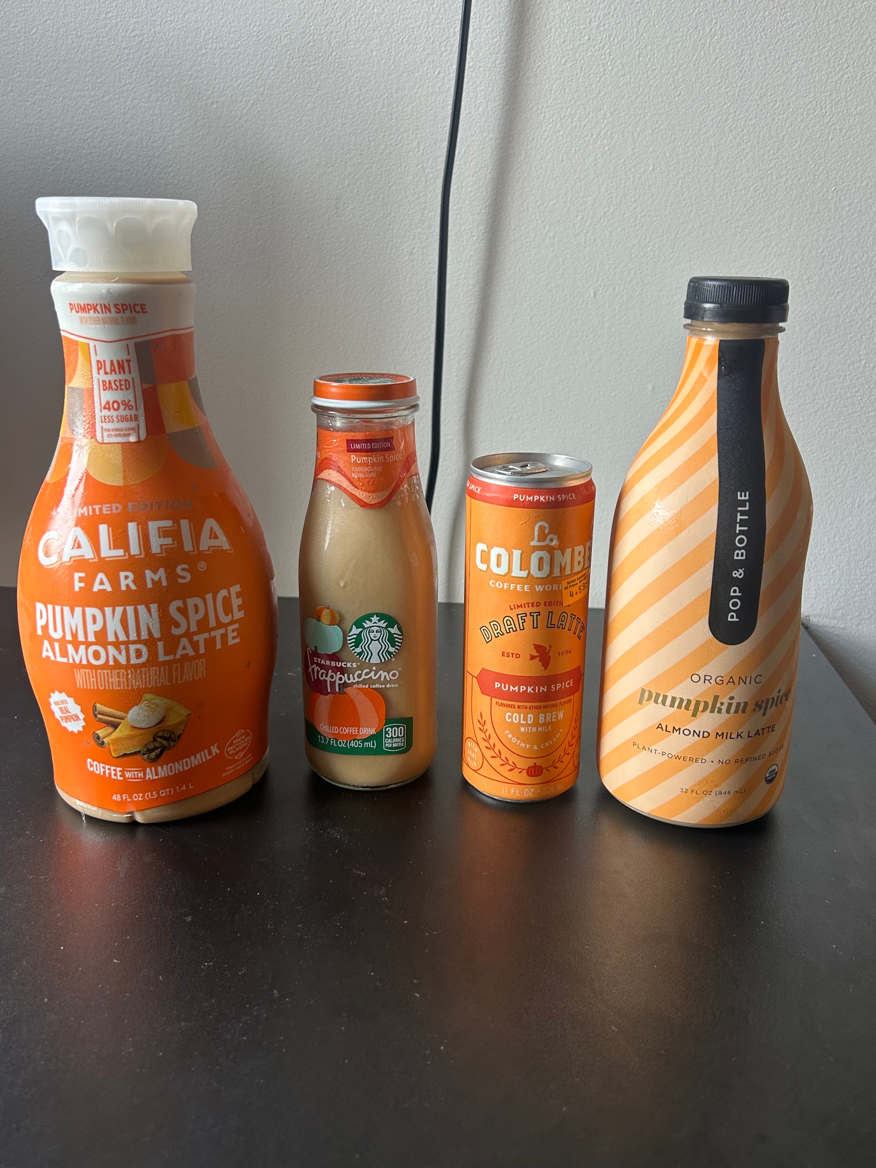 Four pumpkin spice beverage containers on a table: almond latte, frappuccino, draft latte, and almond milk latte