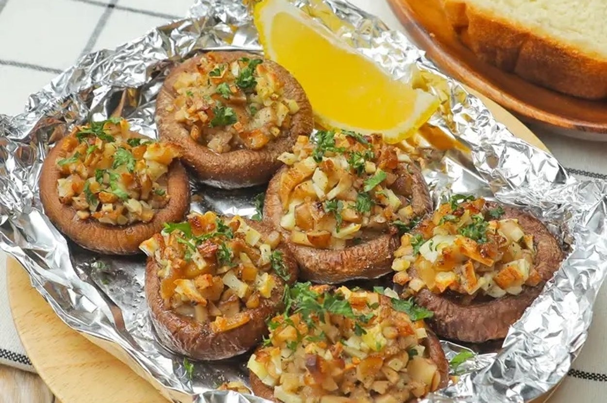 ホイルに包まれた香草とパン粉を乗せた焼きポートベロマッシュルームが木の皿に盛られ、レモンとパンが添えられている。