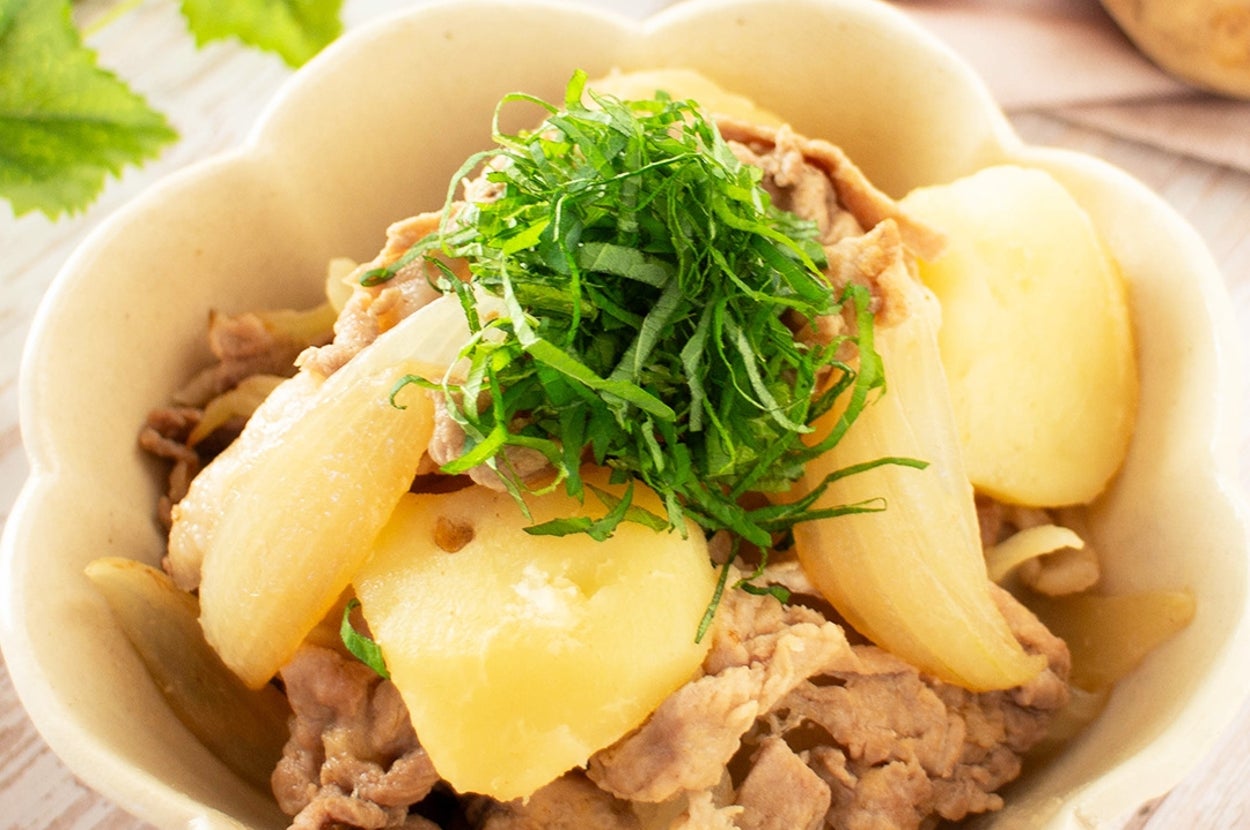 肉じゃがの盛り付け。薄切りの肉とじゃがいも、玉ねぎに青じそのトッピングがされている。白い器に盛られている。